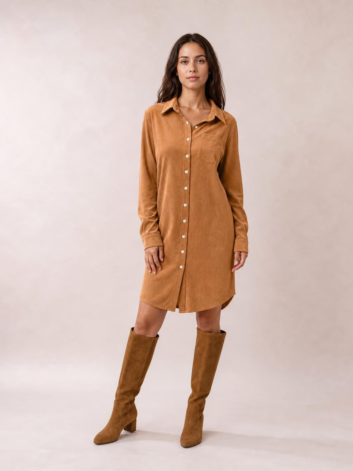 Model stands in a camel corduroy shirt dress with a collared neckline, long sleeves, button-down front, chest pocket, and relaxed straight silhouette.