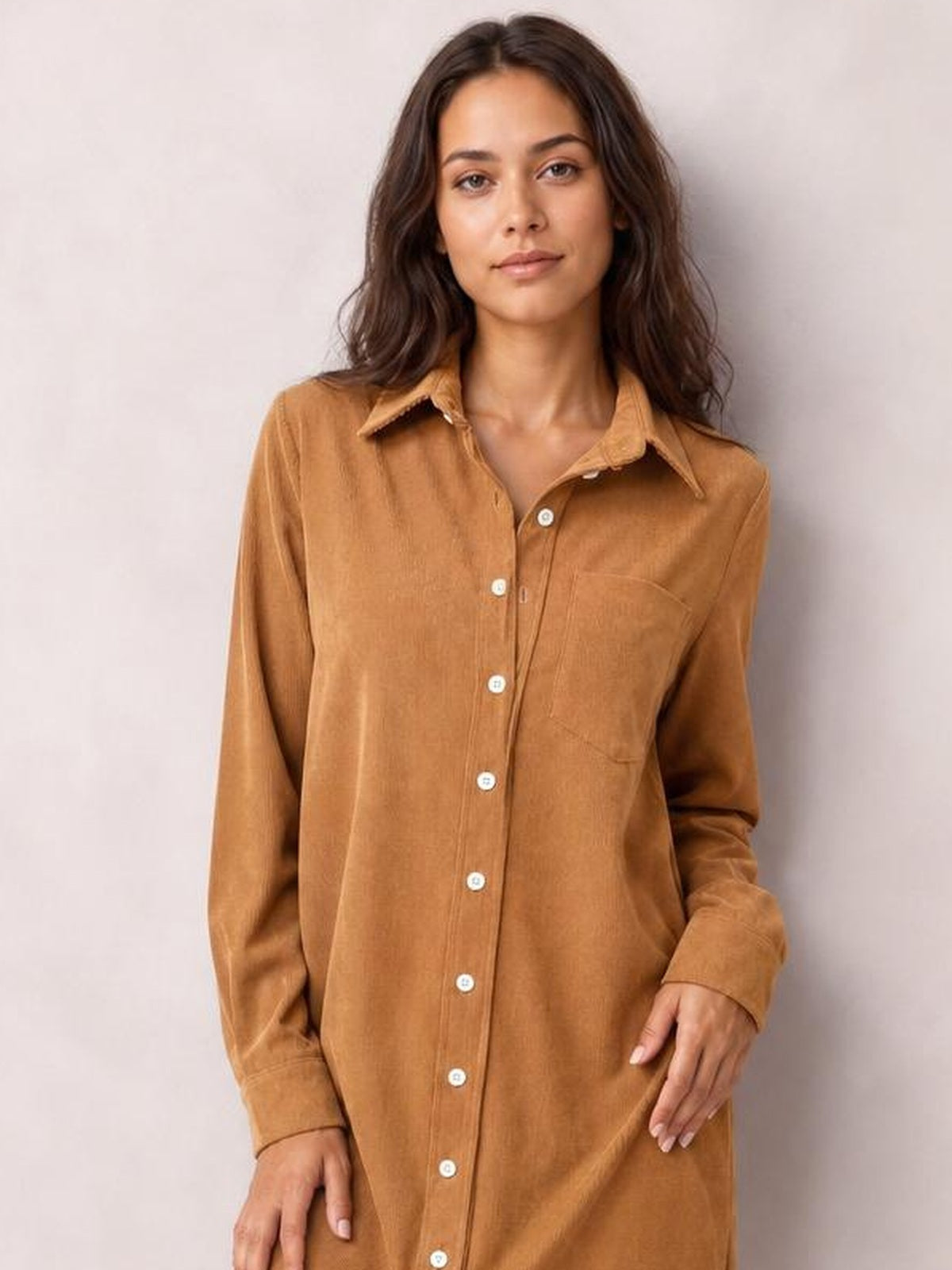 A model stands in a camel-brown corduroy shirt dress with a collared neckline, long sleeves, button-down front, chest pocket, and relaxed straight silhouette.