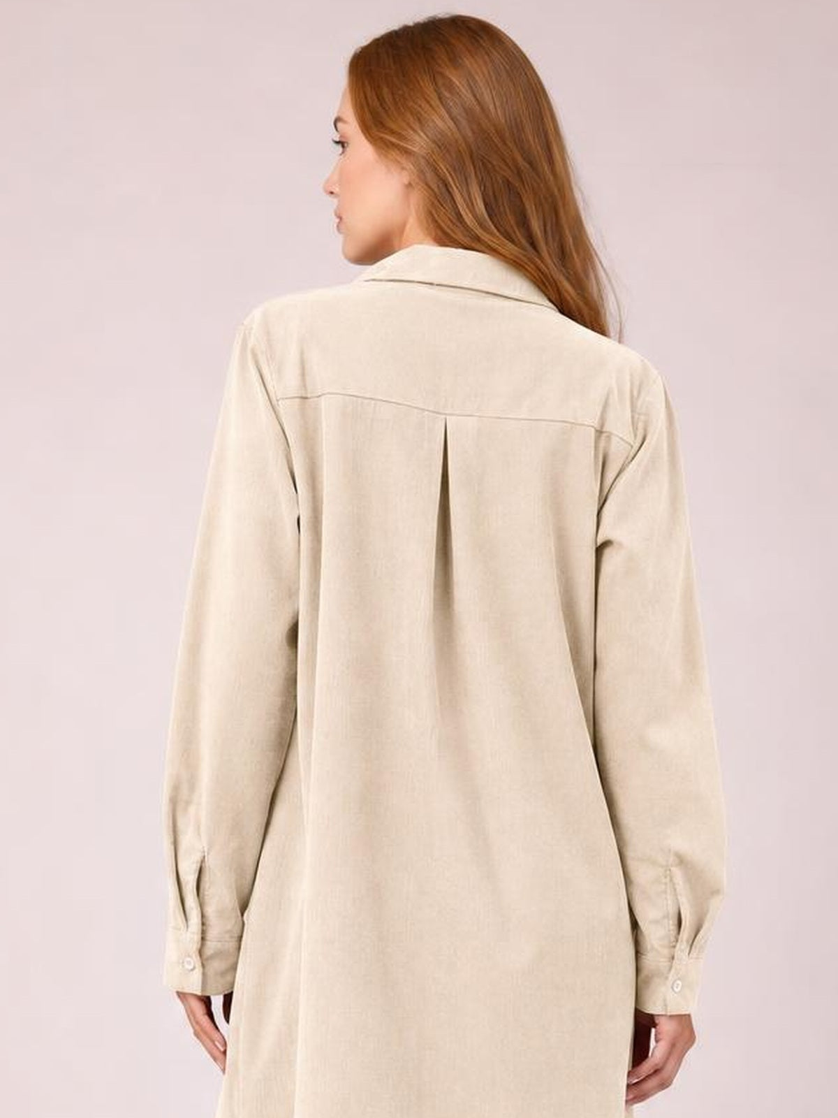 Model shown from the back in a cream corduroy shirt dress with a collared neckline, long sleeves, button cuffs, back yoke, center pleat, and relaxed straight silhouette.