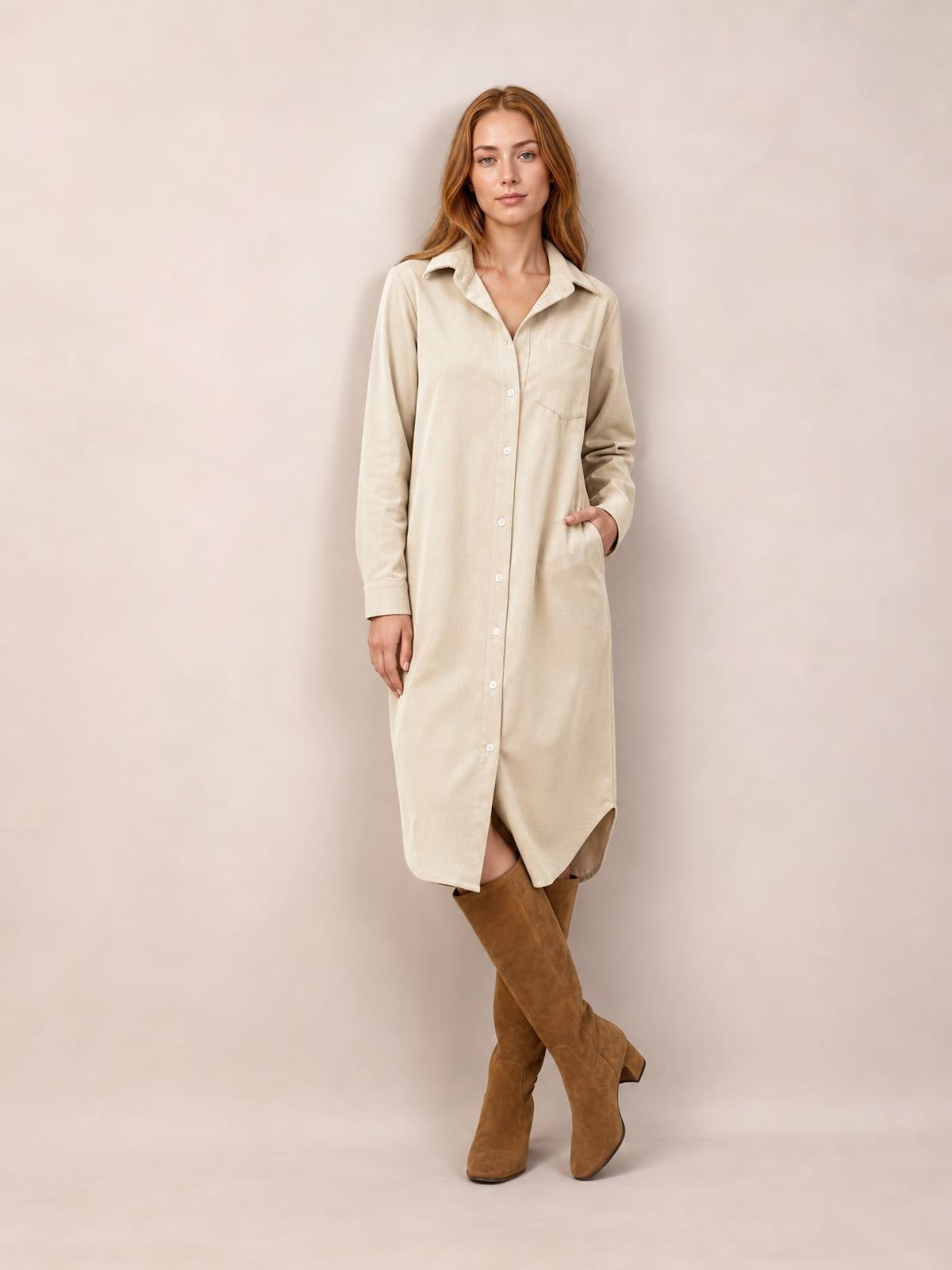 A model wears a cream corduroy shirt dress with a button-down front, pointed collar, long sleeves, chest and side pockets, and a relaxed midi silhouette.