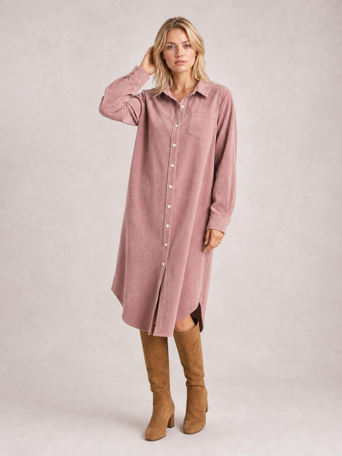 A model poses in a dusty pink corduroy shirt dress with a button-down front, collared neckline, long sleeves, chest pocket, and relaxed straight silhouette.