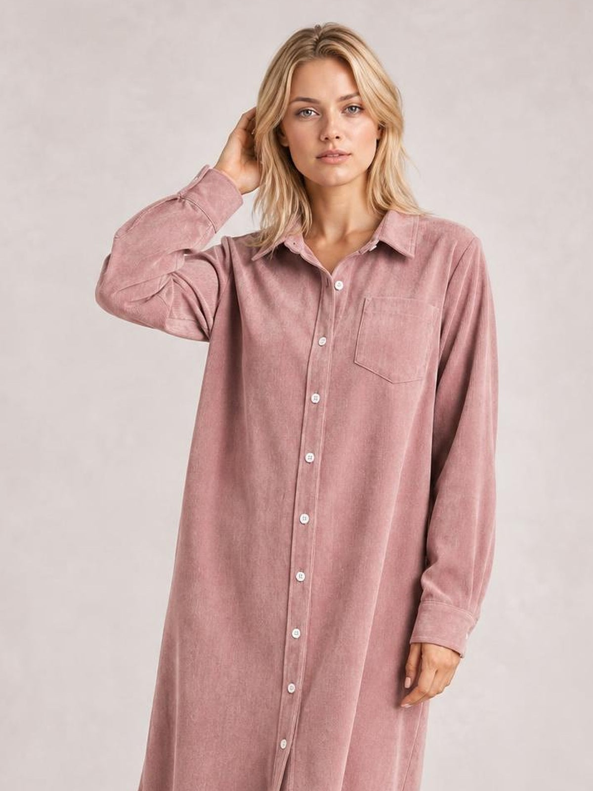 Model poses in a dusty pink corduroy shirt dress with a relaxed straight silhouette, long sleeves, button-down front, collared neckline, and chest pocket.