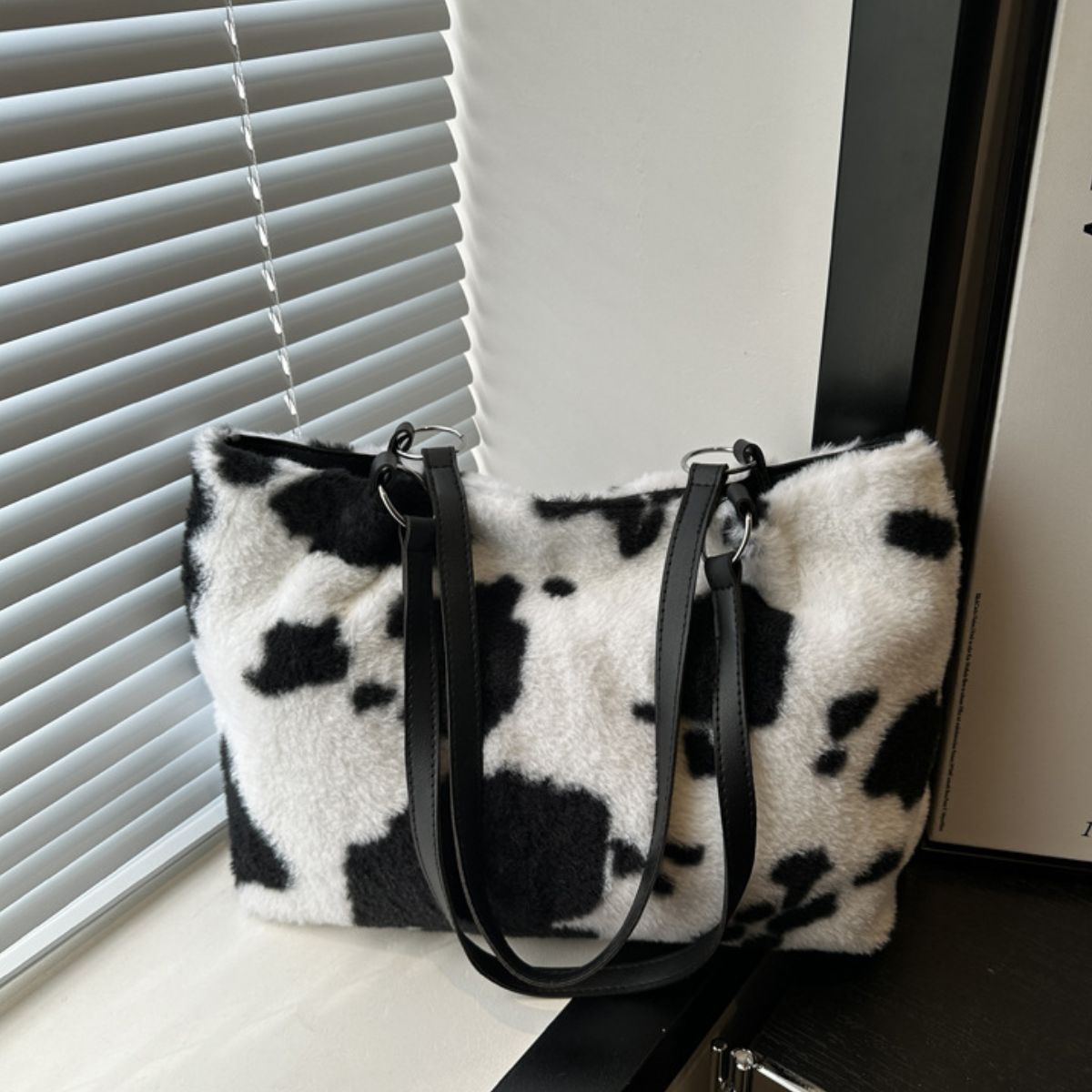 Large cow print furry tote bag with a soft white-and-black faux-fur exterior, clean rectangular silhouette, and long black PU leather shoulder straps.