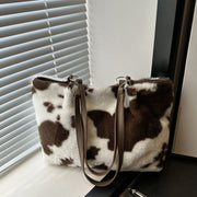 Cow print furry tote bag in a large rectangular silhouette with soft white and brown faux fur, contrasting PU leather trim, and long shoulder straps.
