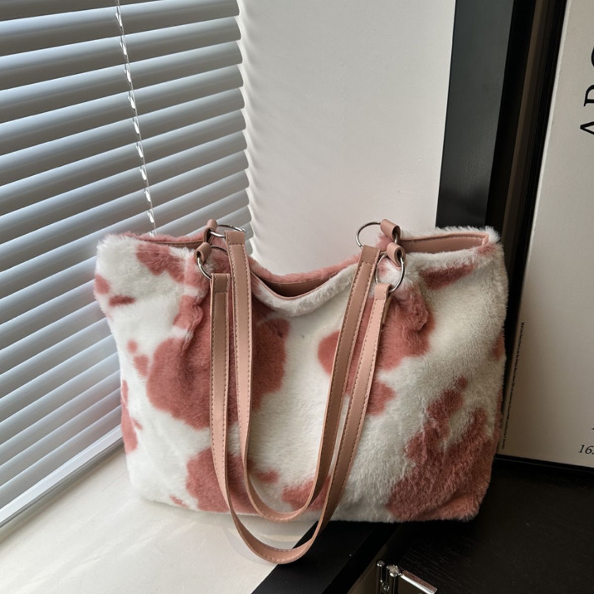 A large pink-and-white cow print furry tote bag features a soft faux-fur exterior, rectangular silhouette, and long pink PU leather shoulder straps.