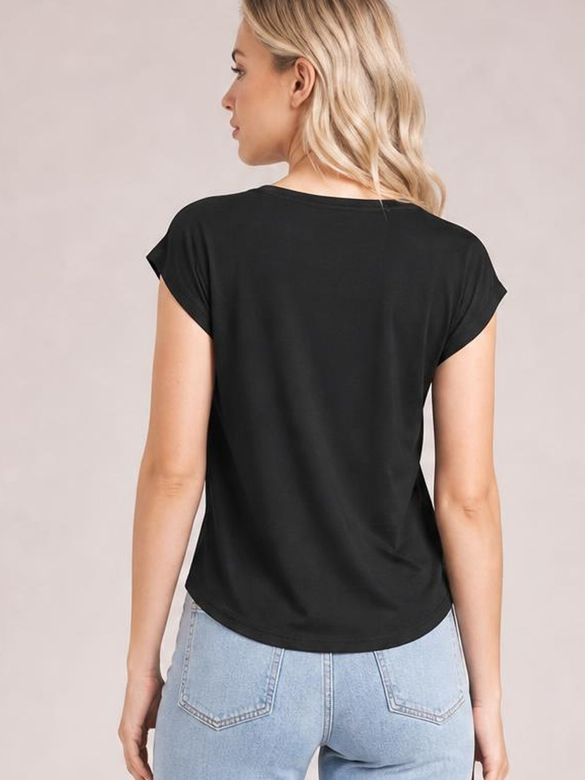 A model is shown from behind wearing a black short-sleeve T-shirt with rolled sleeve cuffs, a relaxed silhouette, and a straight hem.