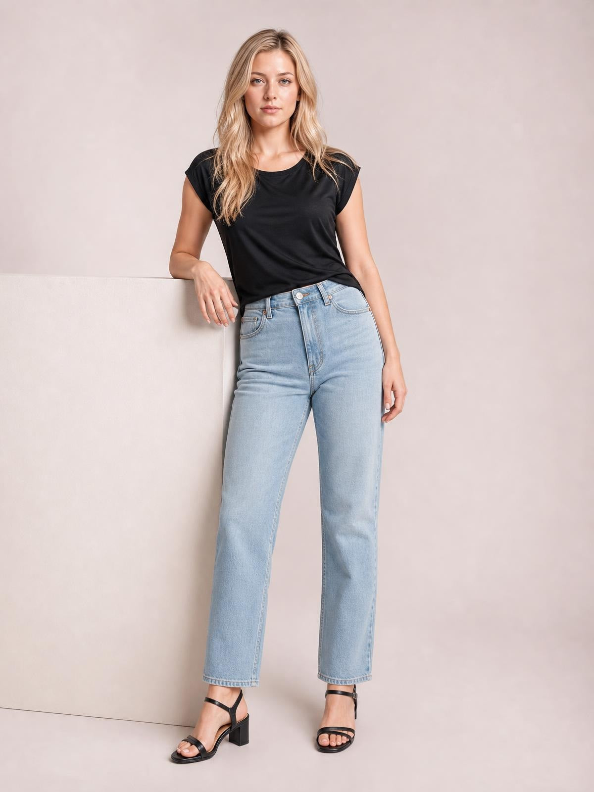 A model poses in a black cowl neck short sleeve T-shirt with a softly draped neckline and relaxed silhouette, paired with light-wash jeans.