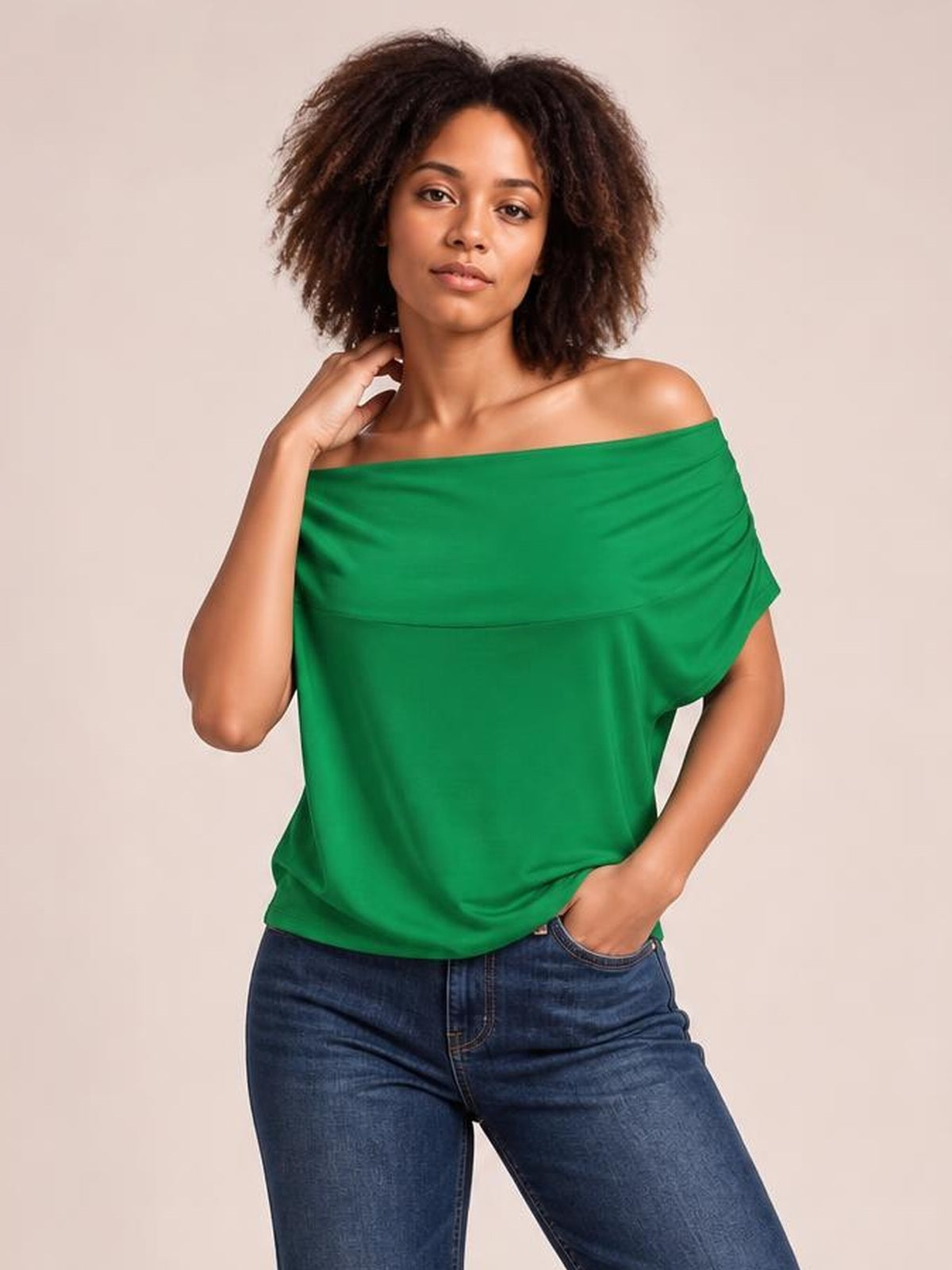 Model poses in a green cowl neck short sleeve T-shirt with an elegant draped, loose silhouette, one hand at her neck and the other in her jeans pocket.