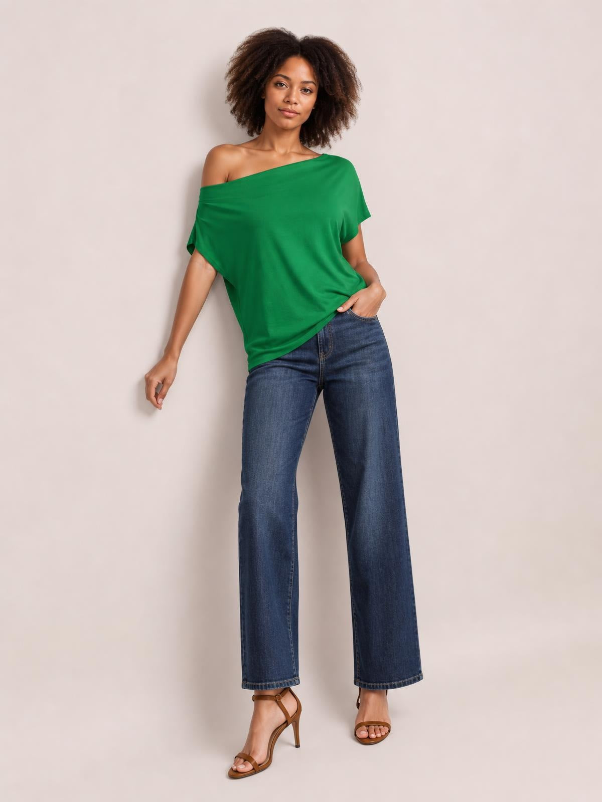 A model poses in a draped green cowl neck short sleeve T-shirt with a relaxed, loose silhouette and wide off-shoulder neckline.