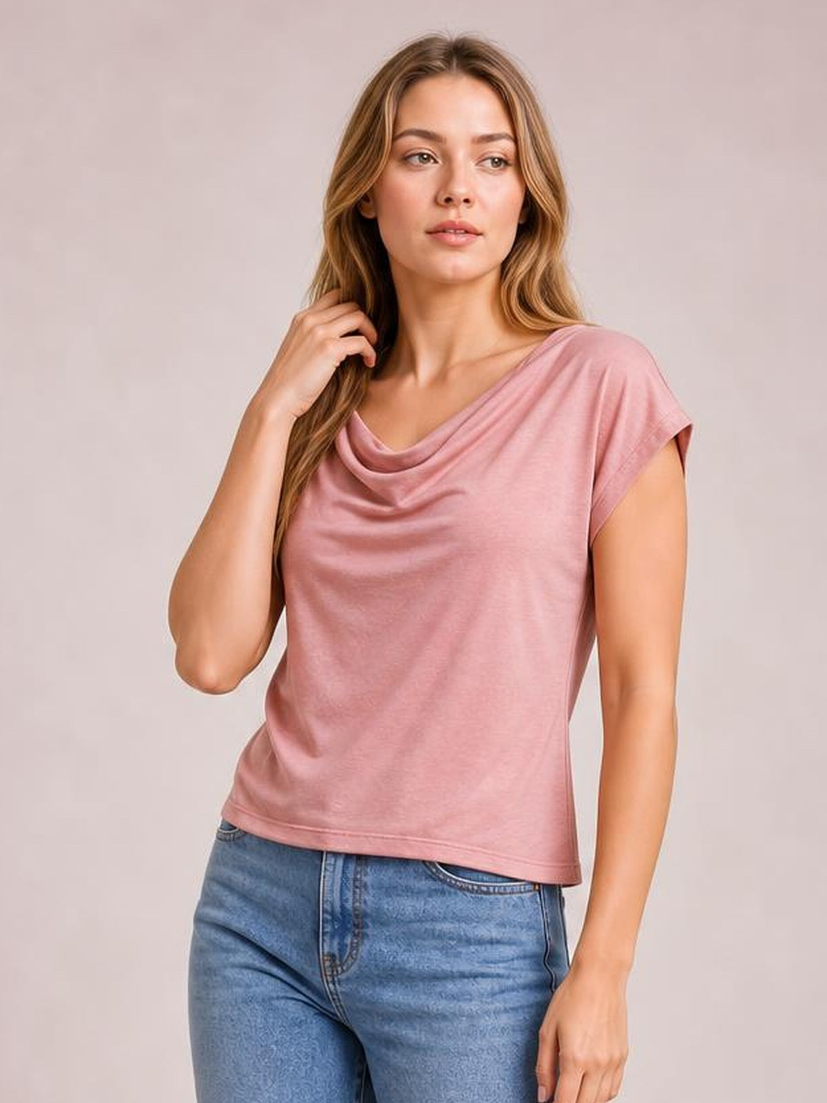 Model wearing a pink cowl neck short sleeve T-shirt with an elegant draped neckline, relaxed silhouette, and straight hem, touching her hair.
