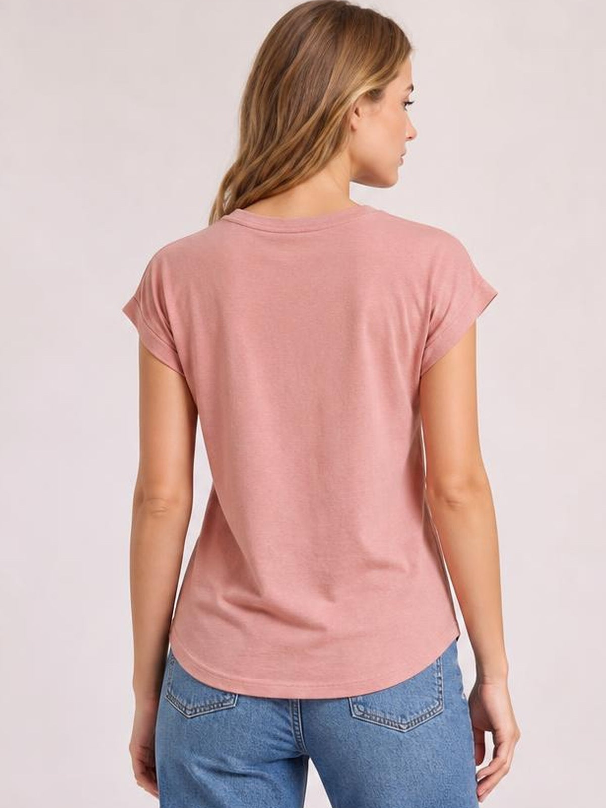 A model is shown from the back in a dusty pink short-sleeve T-shirt with rolled cuffs, a relaxed silhouette, curved hem, and smooth construction.