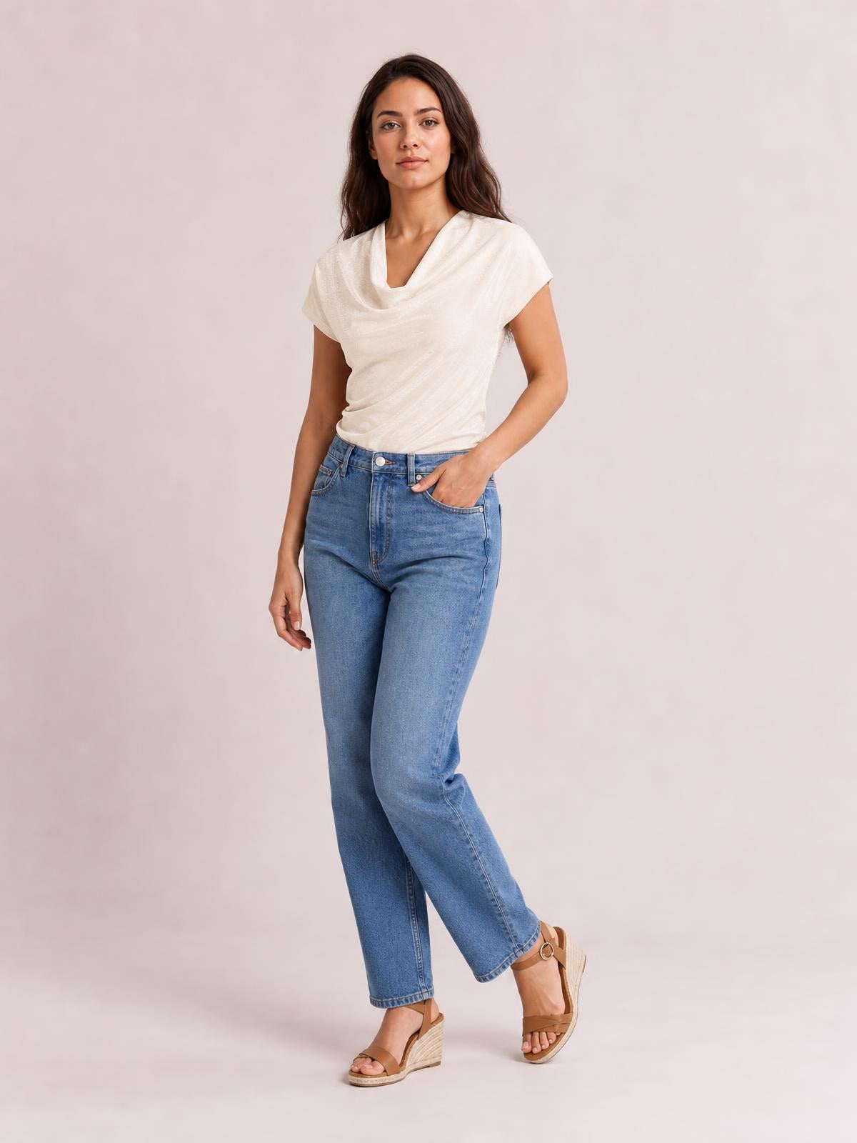 Model wearing an ivory cowl neck short sleeve T-shirt with a softly draped neckline and fitted silhouette, posed with one hand in her jeans pocket.