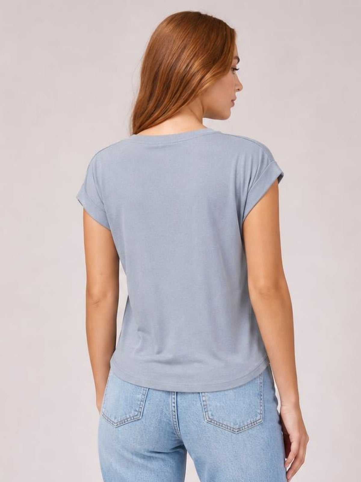 Model shown from the back wearing a light blue short-sleeve T-shirt with rolled cuffs, a relaxed straight silhouette, and a curved hem.