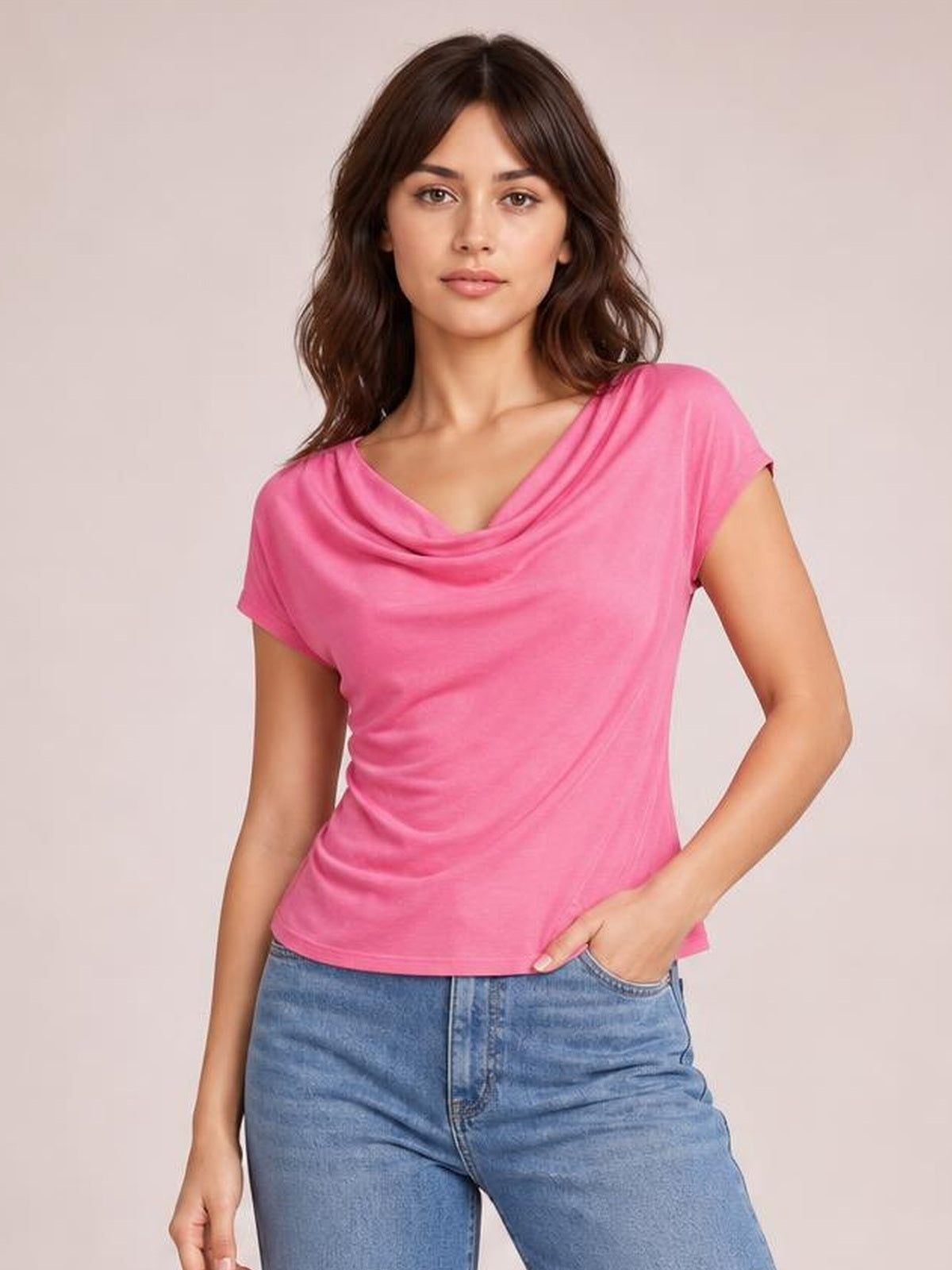 Model wearing a pink cowl neck short sleeve T-shirt with an elegant draped neckline and relaxed silhouette, posing with one hand in her jeans pocket.
