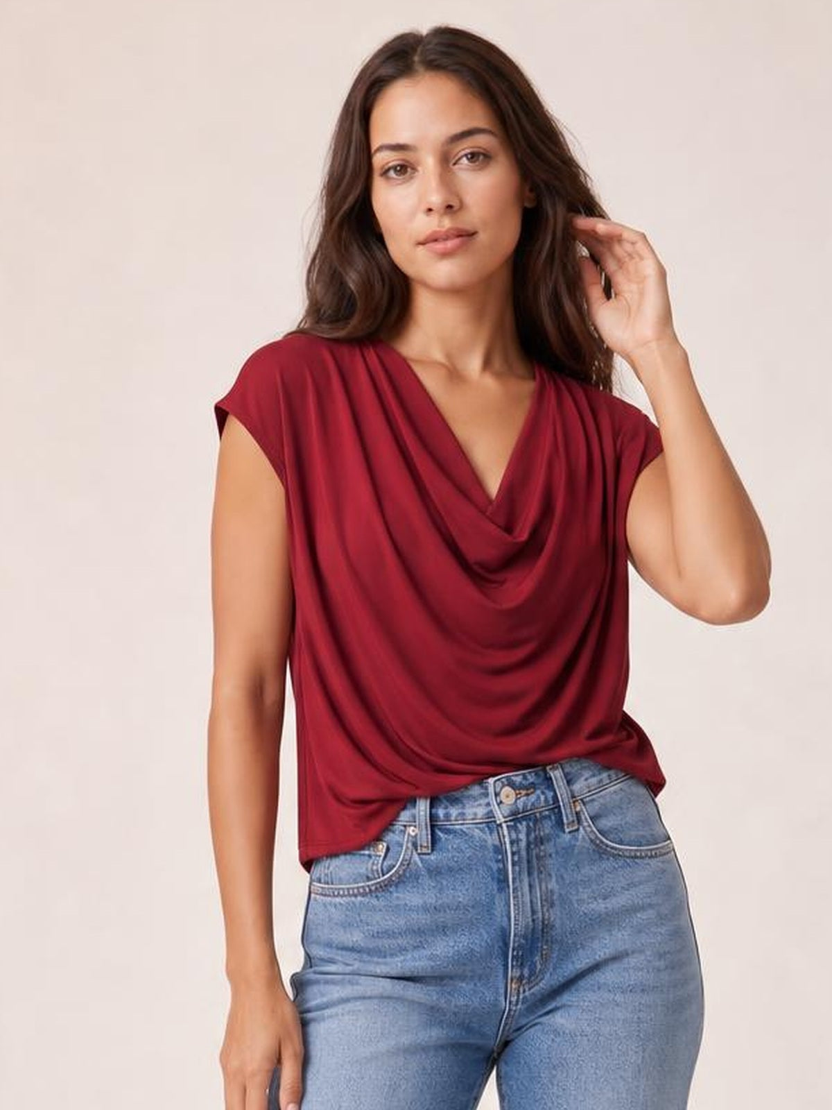 Model wearing a burgundy cowl neck short sleeve T-shirt with an elegant draped neckline and relaxed silhouette, posing with one hand in her hair.