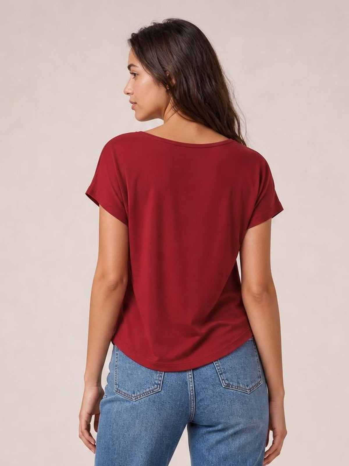 Model looks over her shoulder wearing a burgundy short sleeve T-shirt with a relaxed silhouette, smooth back, cuffed sleeves, and curved hem.