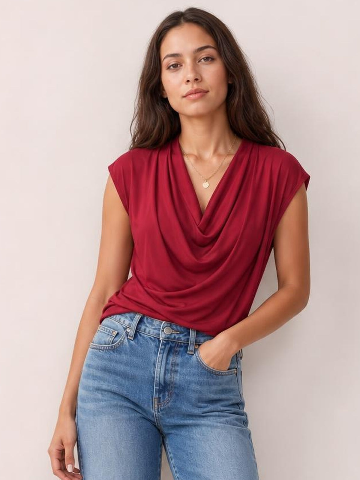 Model wears a burgundy cowl neck short sleeve T-shirt with an elegant draped neckline and relaxed silhouette, posing with one hand in her jeans pocket.
