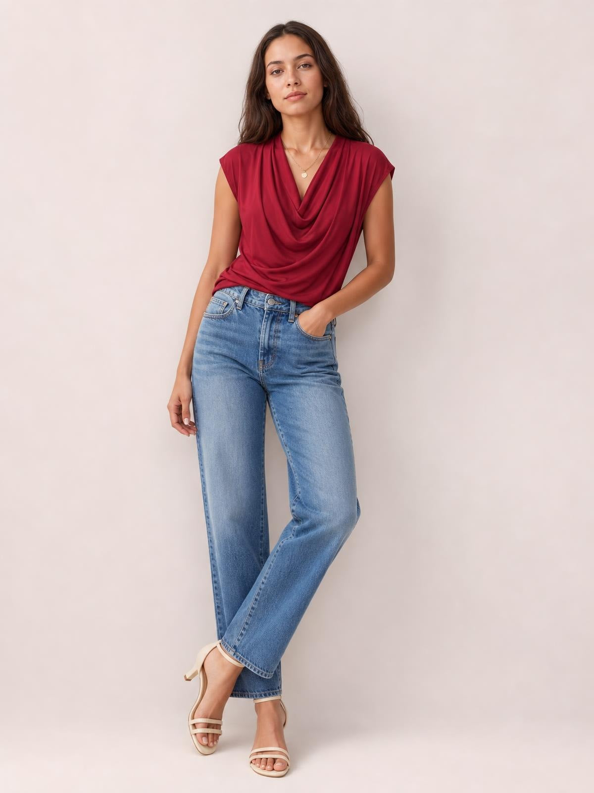 Model wears a burgundy cowl neck short sleeve T-shirt with an elegant draped front and fitted silhouette, posing with one hand in her jeans pocket.