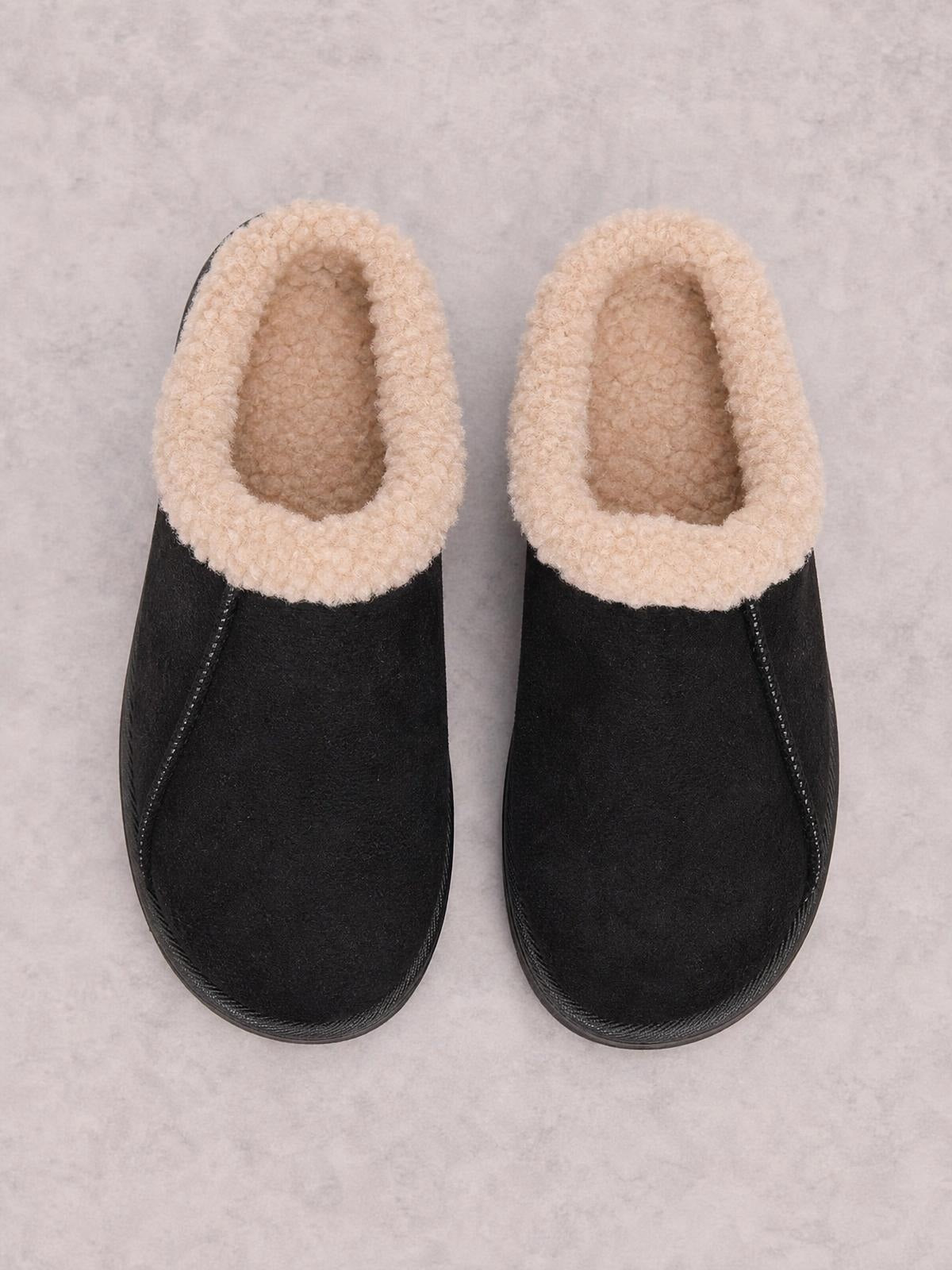Black faux fur lined slippers feature a rounded-toe silhouette, plush cream lining, flat soles, and neat contrasting stitching along the PU leather uppers.