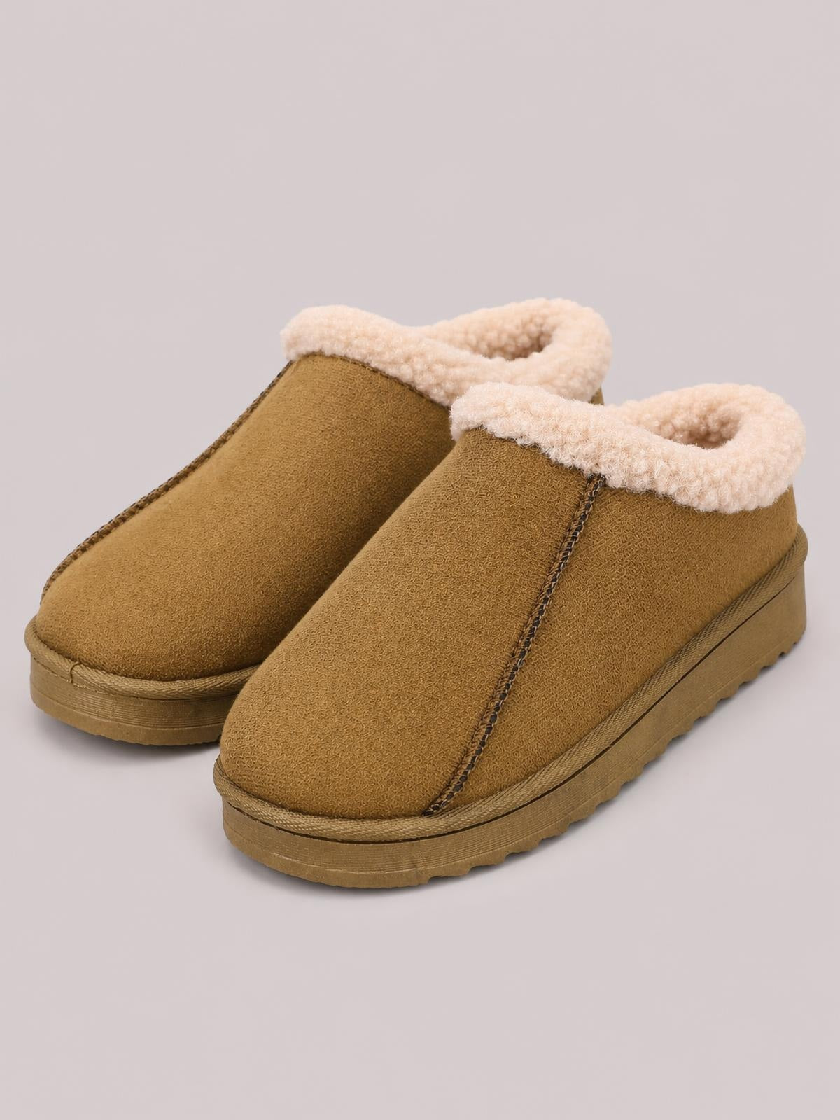 Tan suede slippers feature rounded closed toes, cozy faux fur lining, visible contrast stitching, and thick flat soles for a sturdy, comfortable silhouette.
