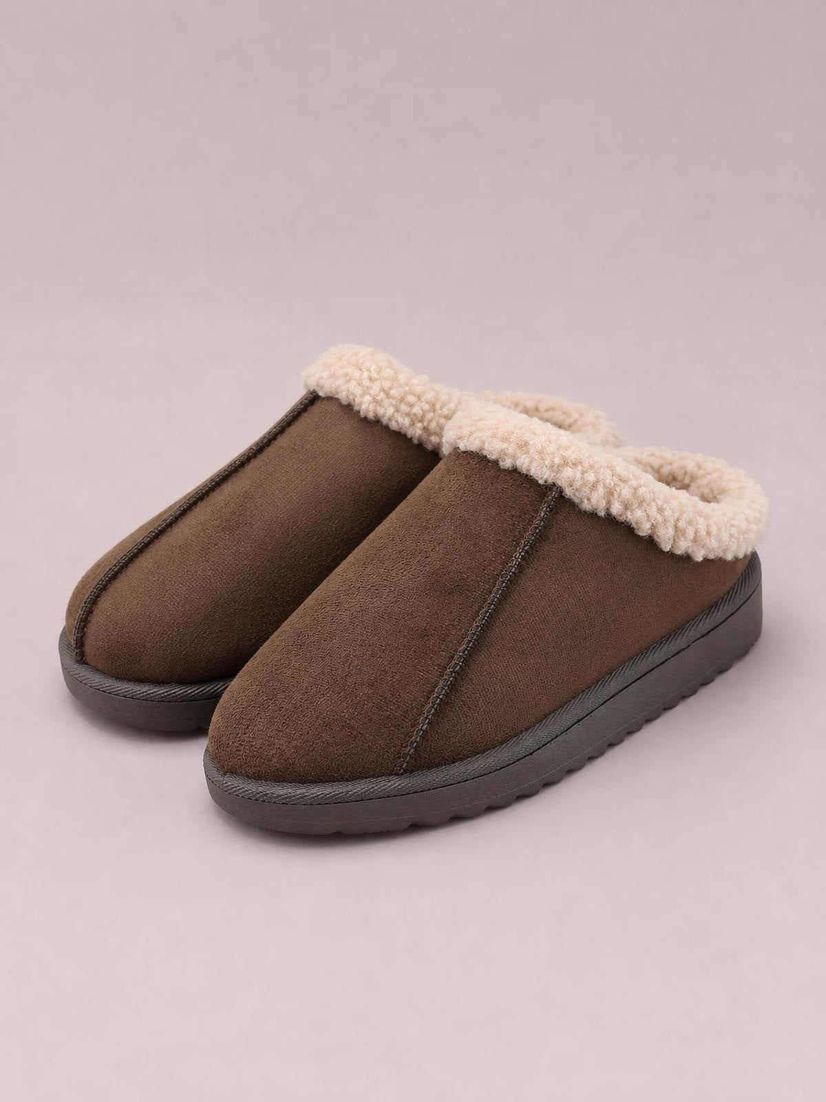 Brown suede-look slippers feature a cozy cream faux fur lining, rounded toes, stitched panel construction, and flat textured lug soles.