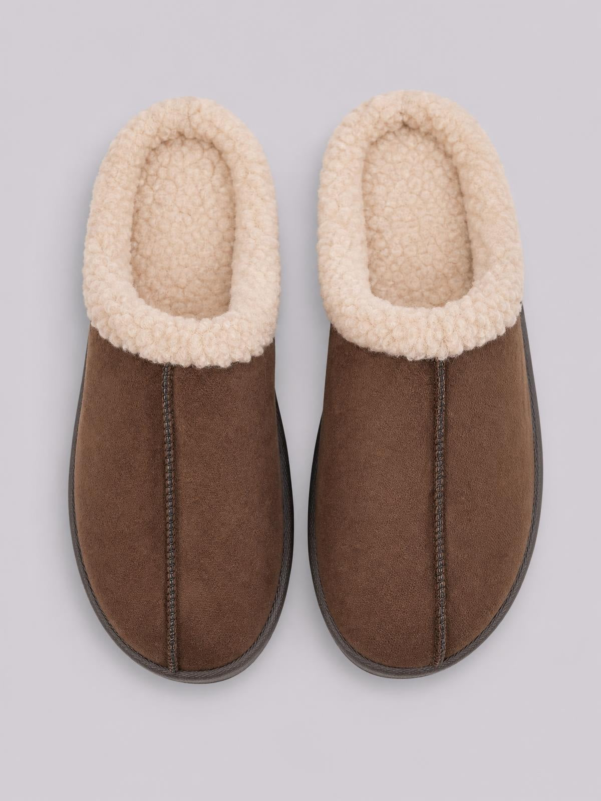 A pair of brown suede slippers with cozy cream faux fur lining, rounded toes, flat soles, and visible center stitching with dark edging.