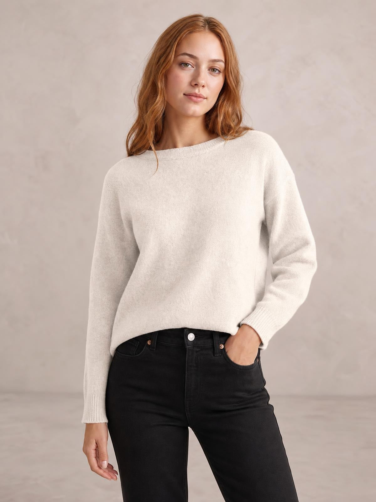 A model poses in a relaxed ivory crew neck long sleeve sweater with a soft knit texture, ribbed cuffs, and a loose straight silhouette.