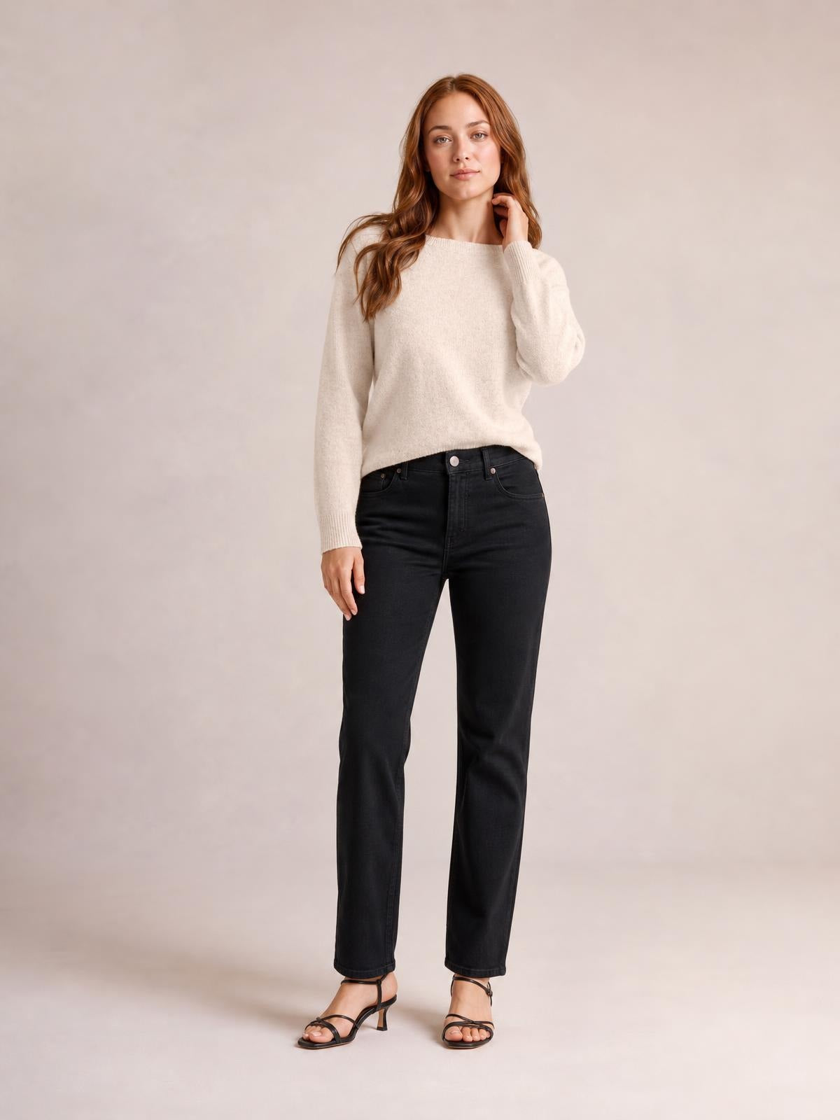 Model wears an ivory crew neck long sleeve sweater with a relaxed silhouette, ribbed cuffs and hem, standing with one hand at her neck.