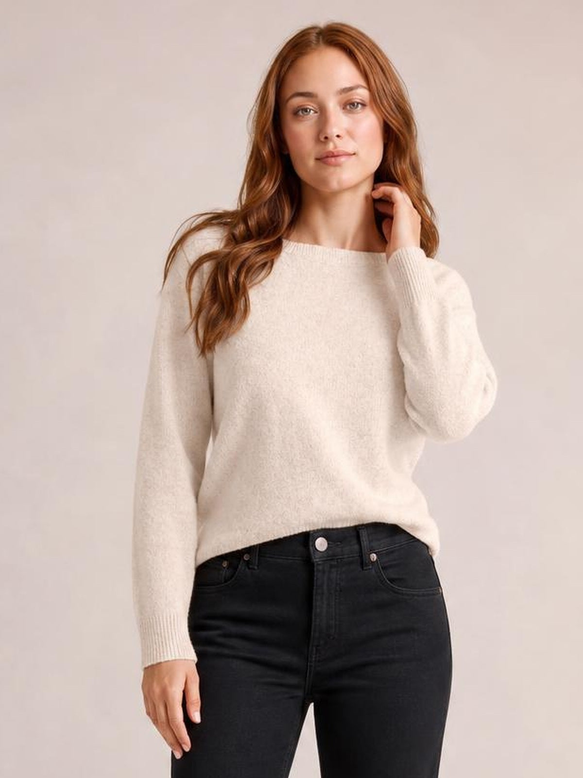Model wearing an ivory crew neck long sleeve sweater with ribbed cuffs and hem, a relaxed silhouette, and a slightly angled pose with one hand near her neck.