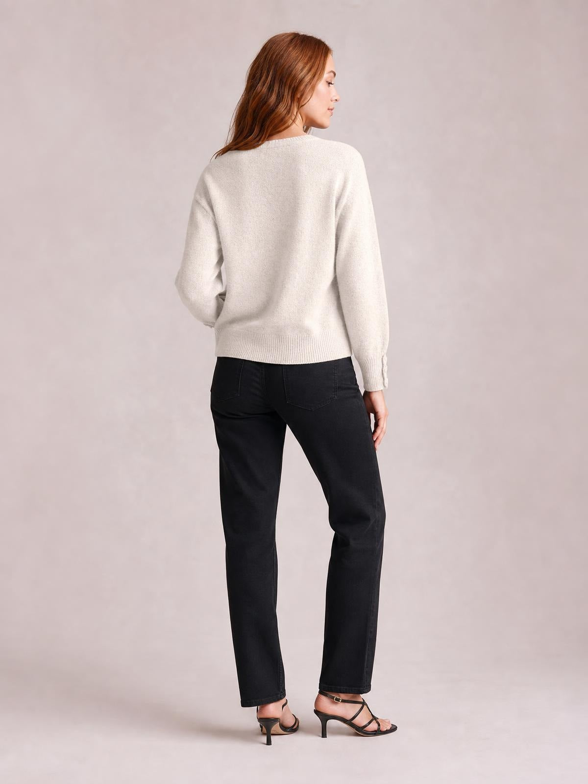 Model shown from the back in a relaxed ivory crew neck long sleeve sweater with a straight silhouette, ribbed hem and cuffs, standing with one hand at her hip.