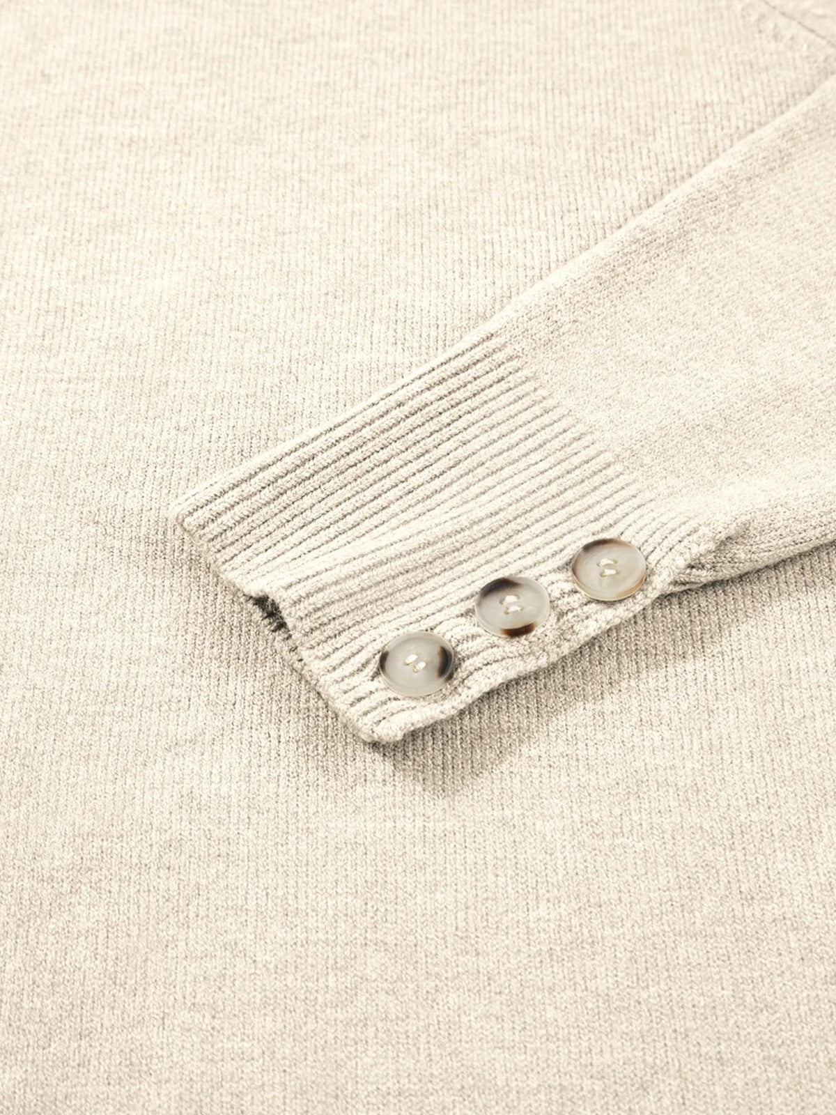 Close-up of a light beige long-sleeve sweater showing a ribbed cuff with three tonal buttons and fine knit texture.