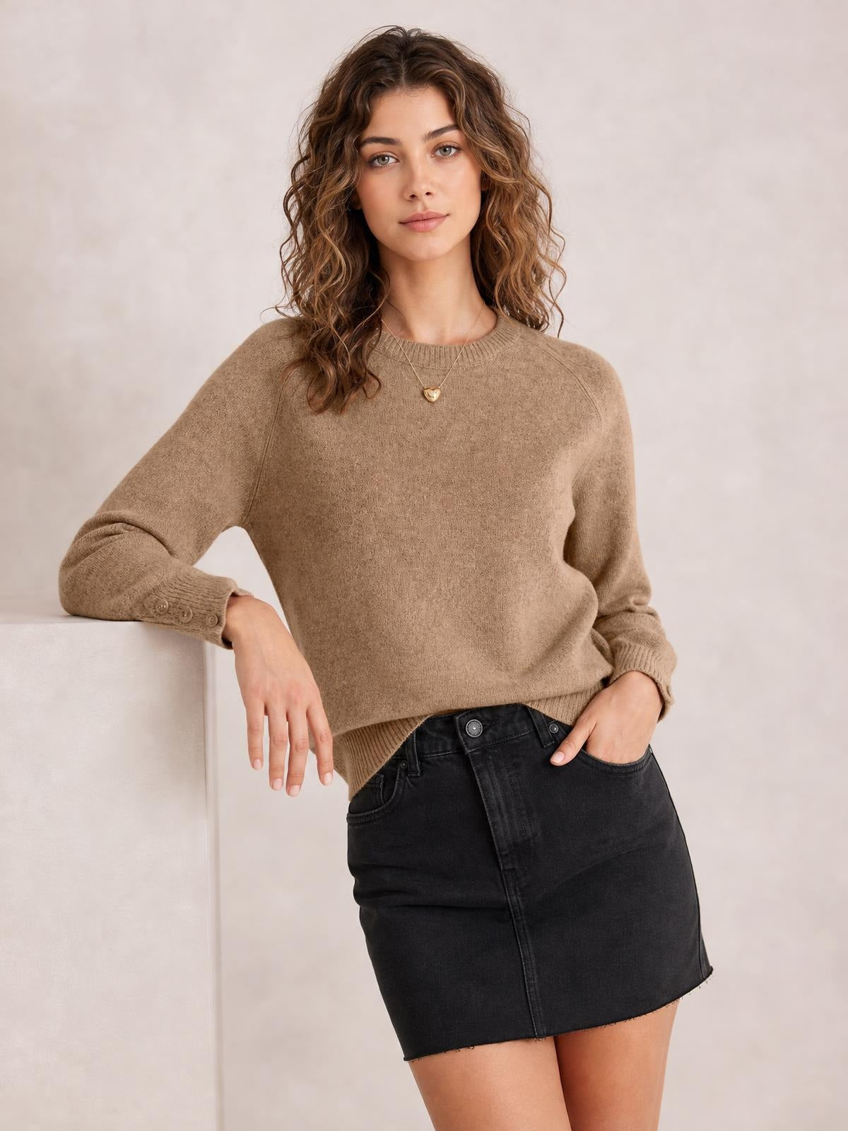 Model wears a taupe crew neck long sleeve sweater with a relaxed silhouette, ribbed cuffs and hem, and button detailing at the cuffs.