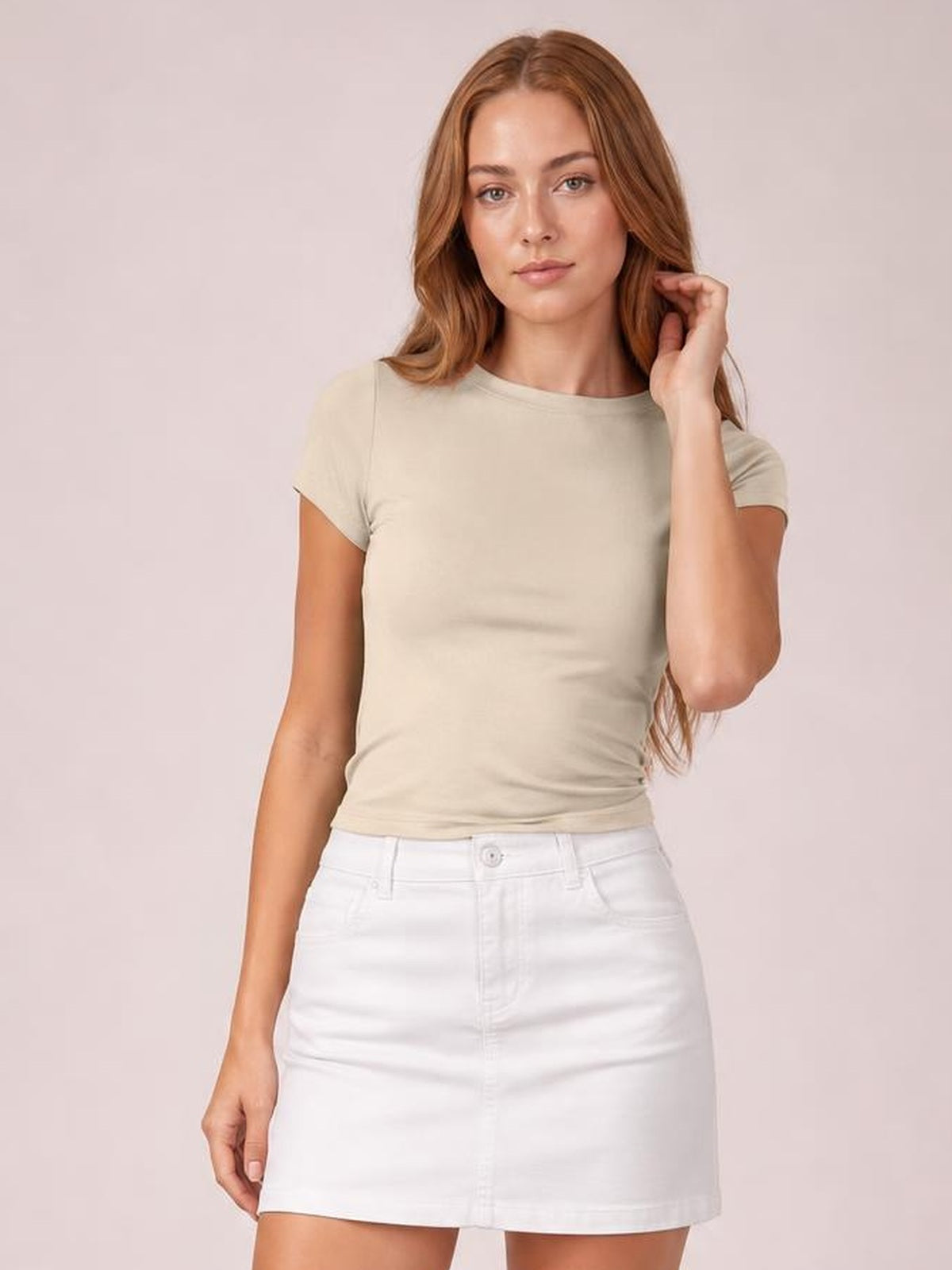 Model in a beige solid crewneck short sleeve tee with a regular silhouette and ribbed round neckline, posing with one hand touching her hair.