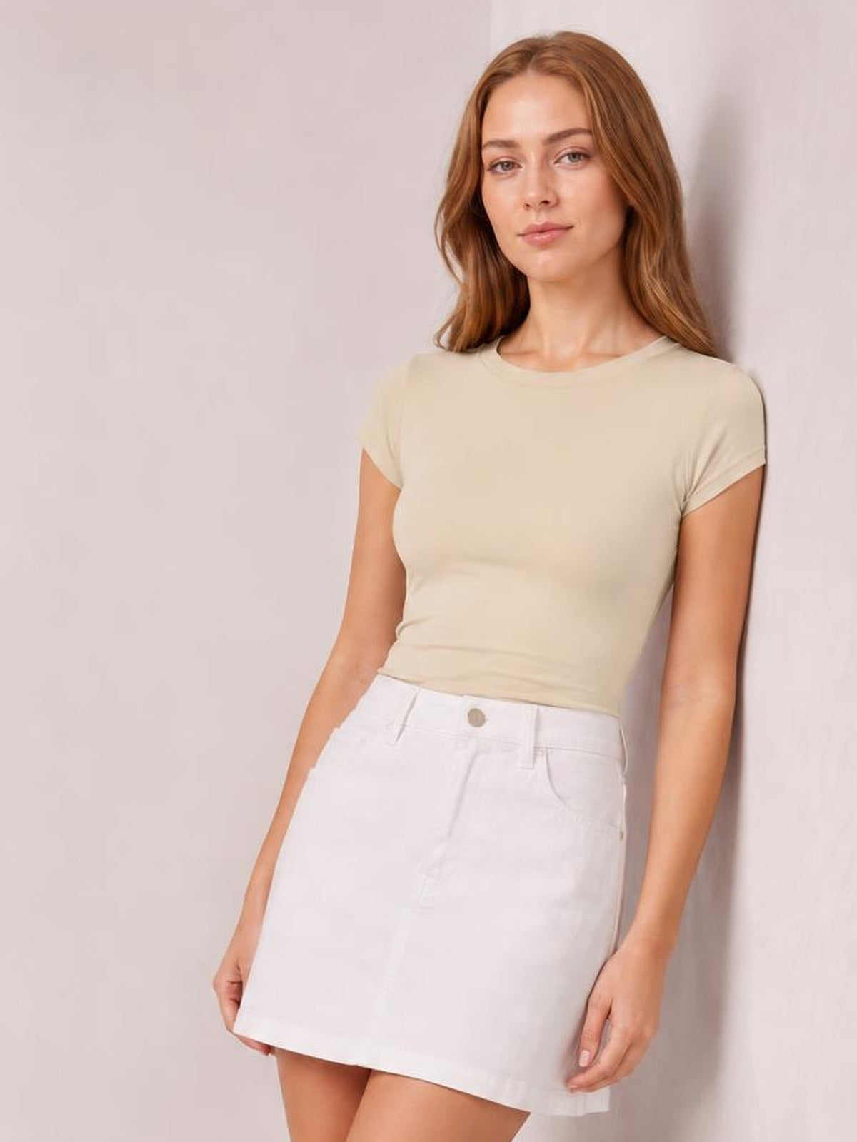 Model leans against a wall wearing a solid beige Crewneck Short Sleeve Tee with a round neck, regular short sleeves, and a fitted regular-length silhouette.