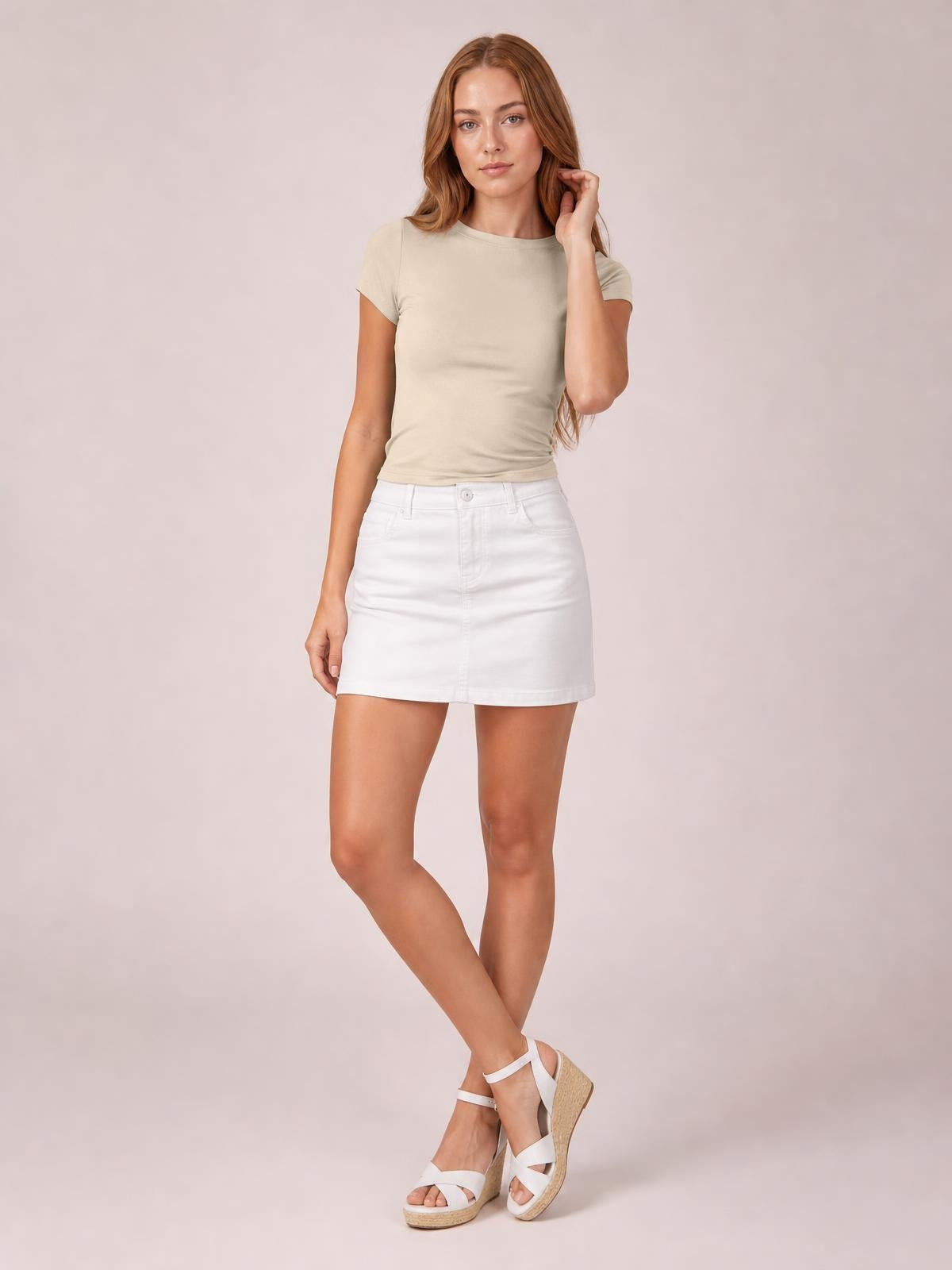 Model wearing a solid beige Crewneck Short Sleeve Tee with a round neck, fitted regular-length silhouette, and short sleeves, posing with crossed legs.