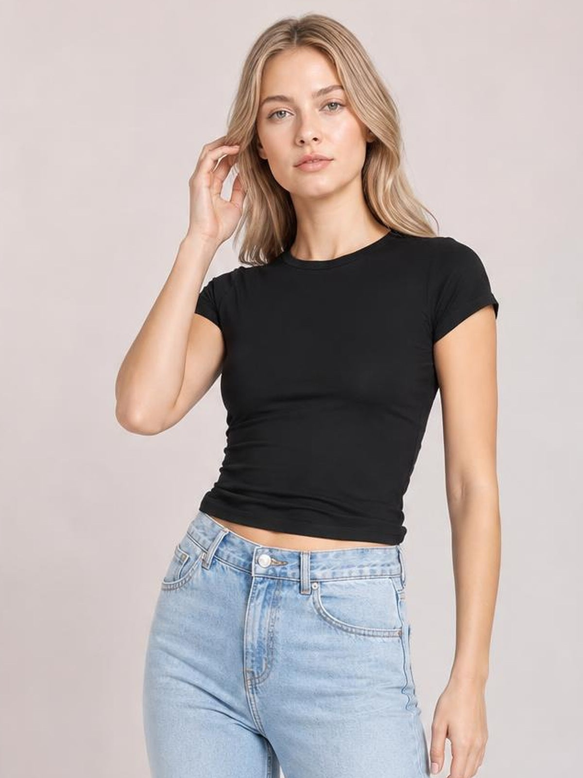 Model poses in a black crewneck short sleeve tee with a fitted silhouette, regular sleeves, and a straight hem, lifting one hand to her hair.