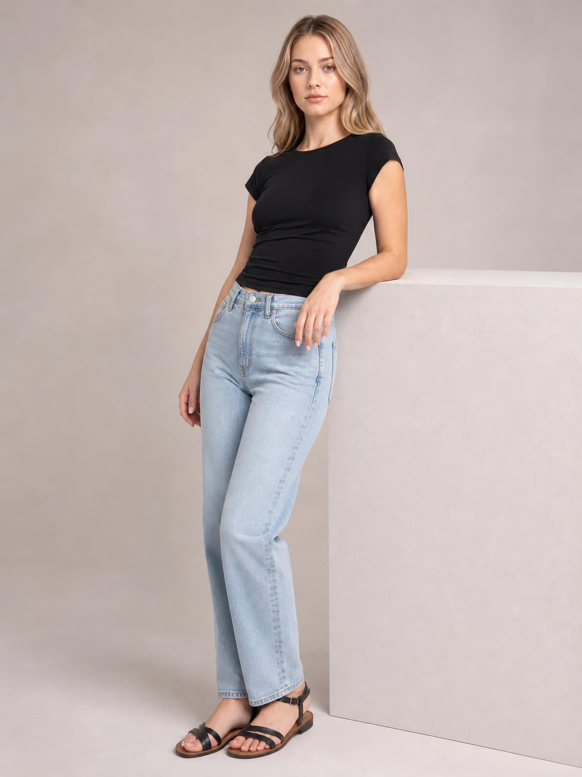 Model wears a black solid crewneck short sleeve tee with a fitted regular-length silhouette and rolled sleeve edges, leaning against a pedestal.