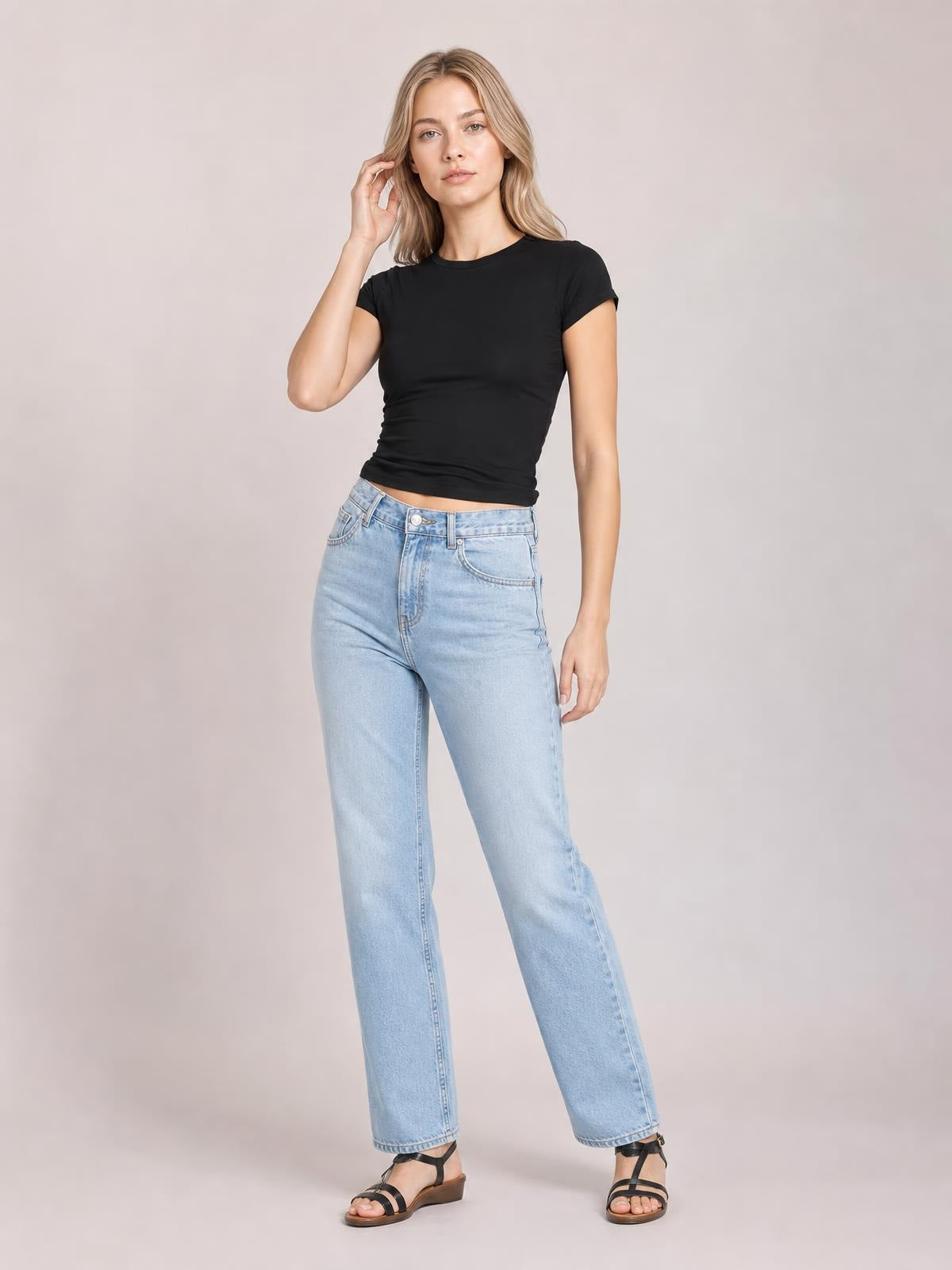 A model poses in a solid black crewneck short sleeve tee with a fitted silhouette and regular length, touching her hair with one hand.