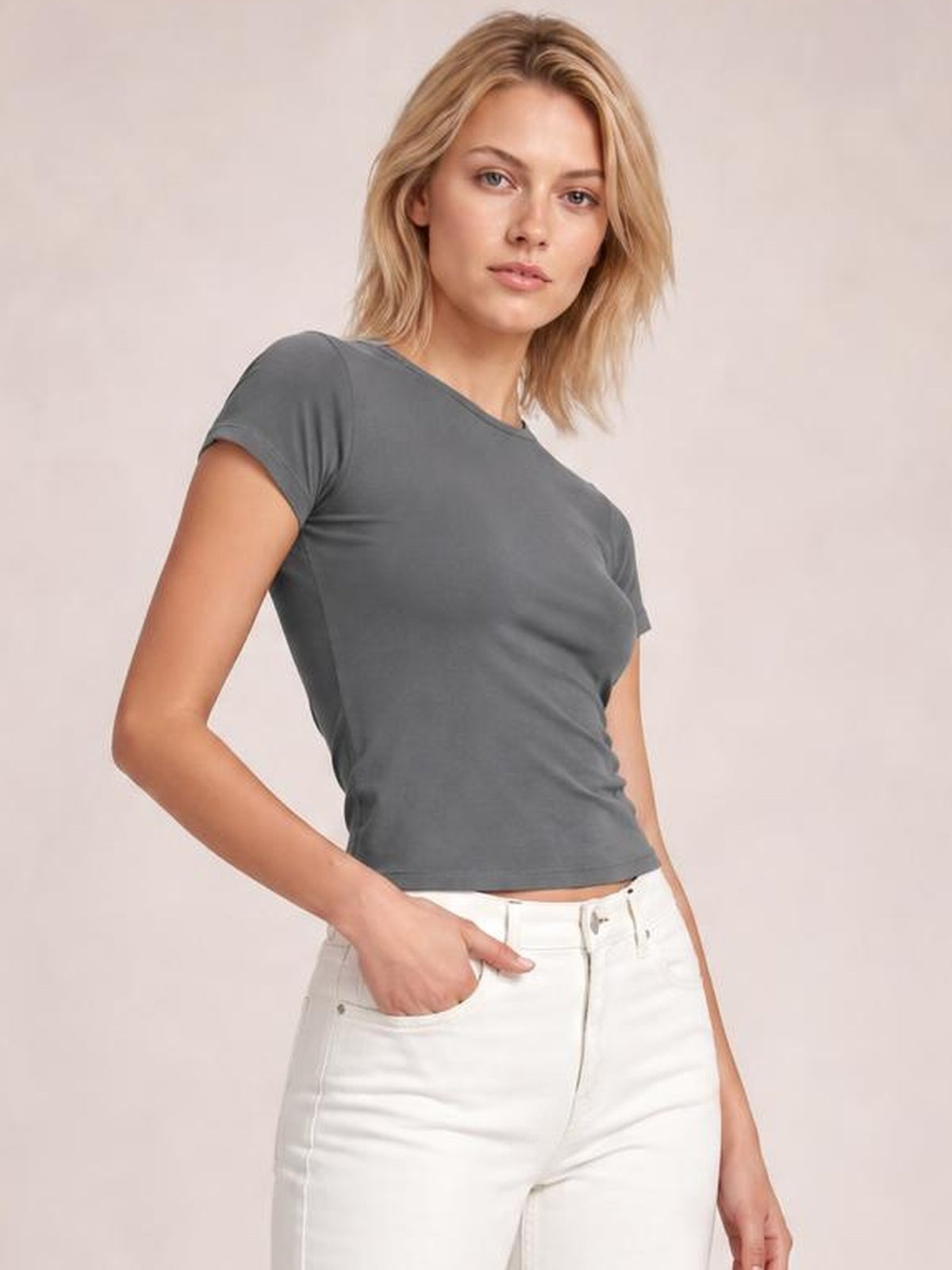 Model wearing a solid gray crewneck short sleeve tee with a fitted regular silhouette, standing with one hand in her white jeans pocket.