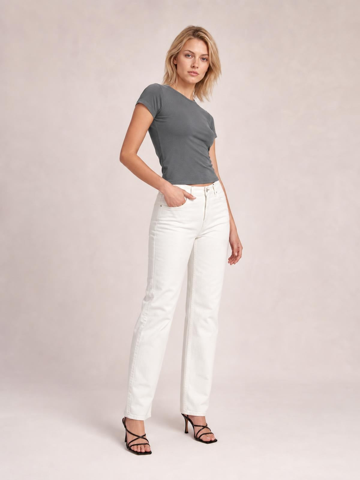 A model poses in a solid gray Crewneck Short Sleeve Tee with a round neckline, fitted silhouette, regular length, and short sleeves, one hand at her pocket.