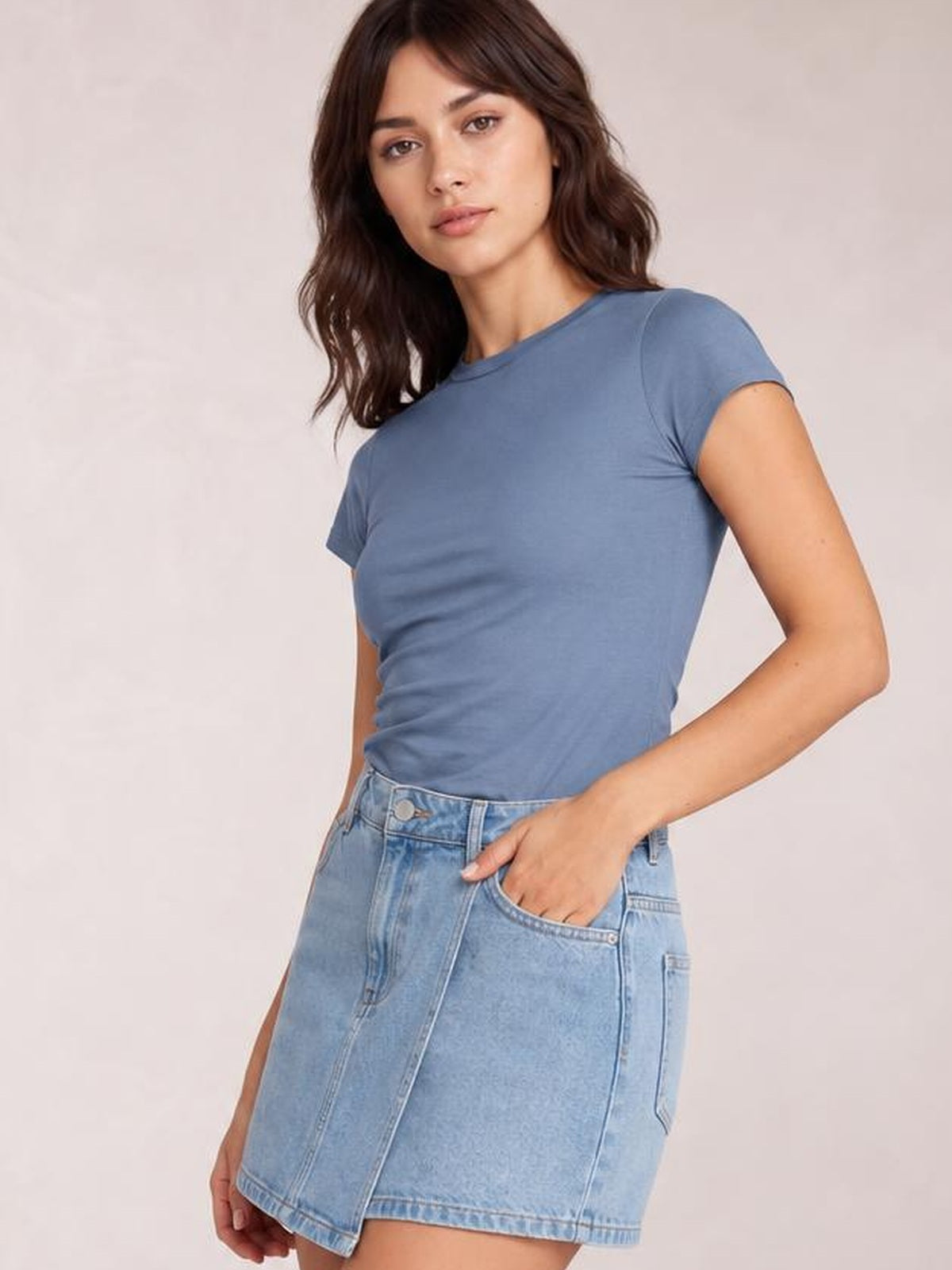 A model poses with one hand in her pocket wearing a solid blue Crewneck Short Sleeve Tee with a round neck, regular length, and close-fitting silhouette.