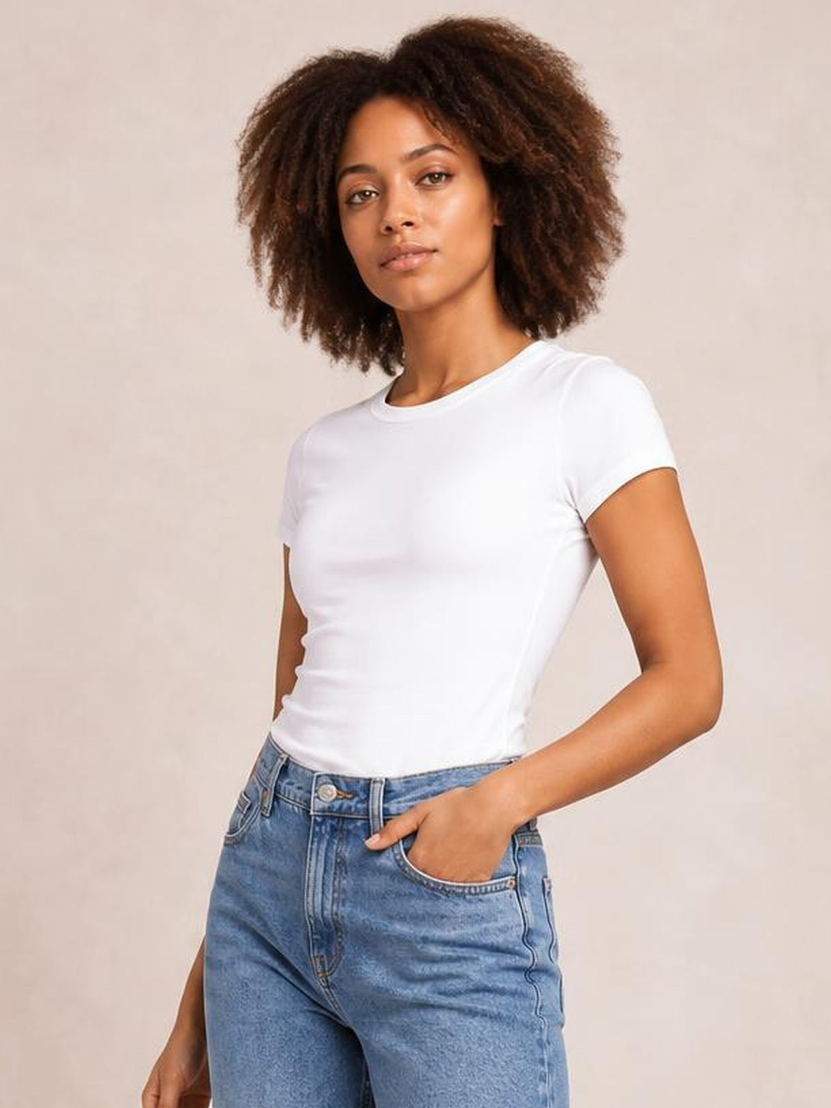 A model wears a white solid crewneck short-sleeve tee with a fitted regular-length silhouette and simple construction, posing with one hand in her jeans pocket.