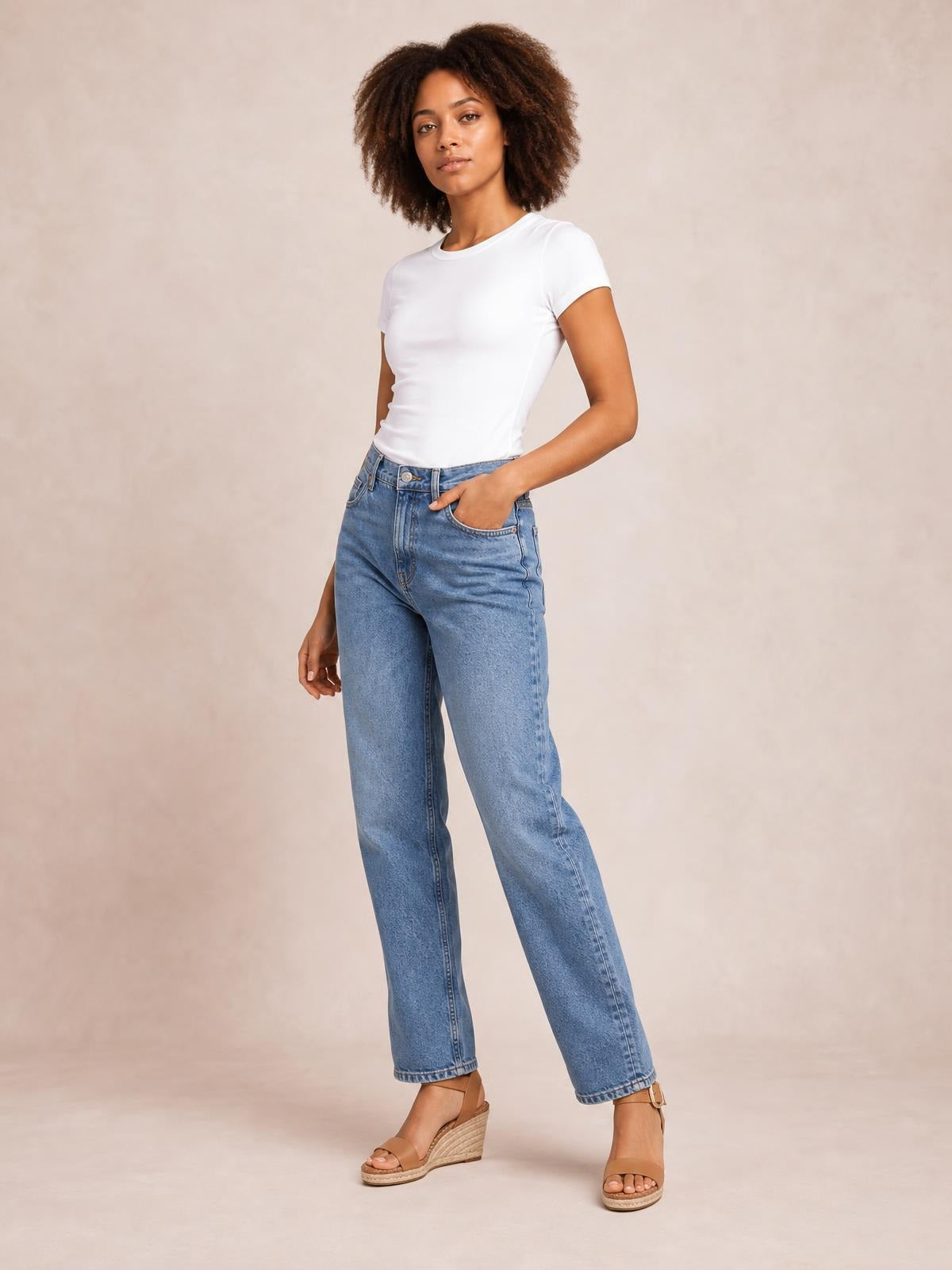 Model poses in a white solid crewneck short sleeve tee with a fitted silhouette and regular length, paired with high-waisted jeans.