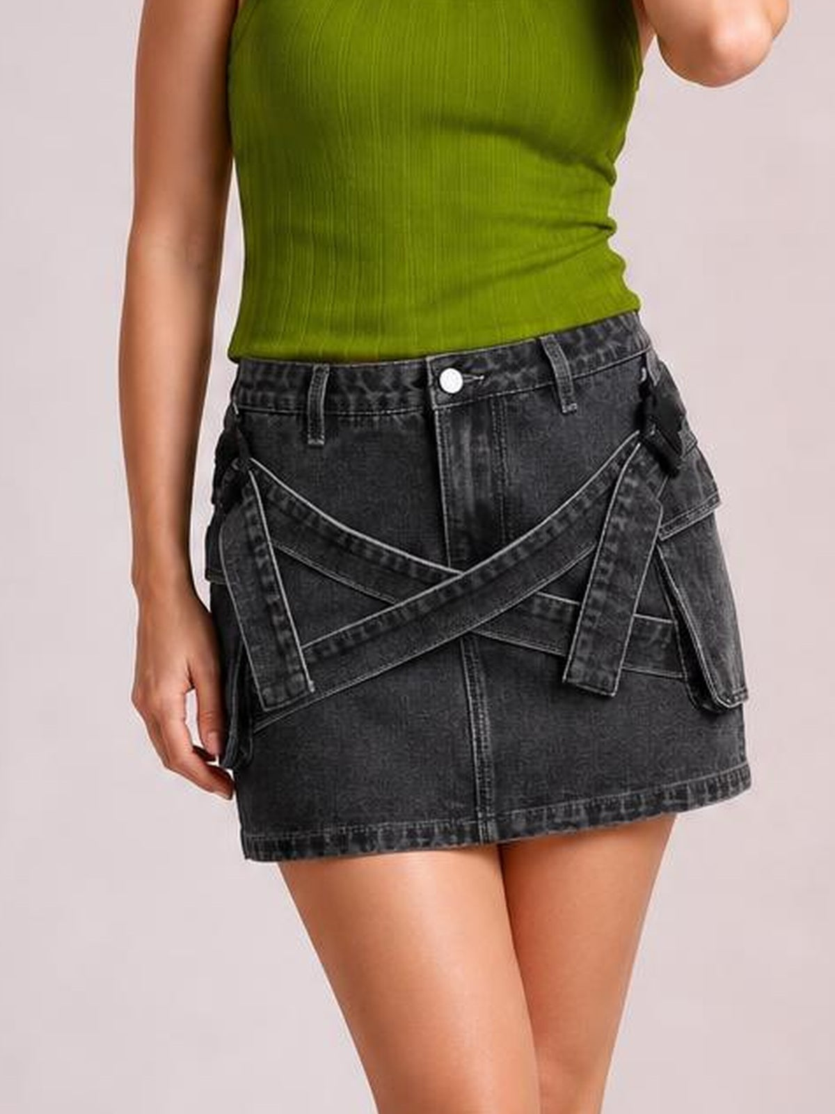 Model wears a black denim mini skirt with a structured hem, pockets, belt loops, and prominent criss-cross waist detail in a straight silhouette.