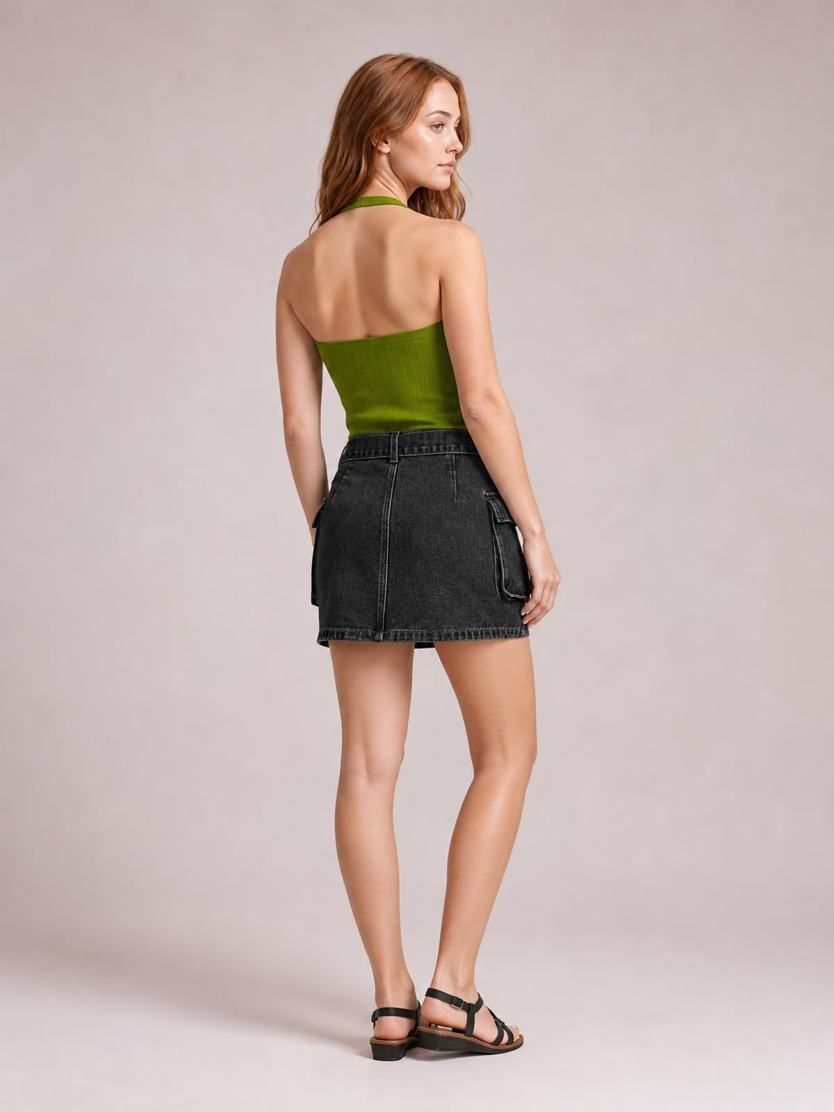 Model poses in a three-quarter rear view wearing a dark denim mini skirt with a high waist, visible pockets, contrast seams, and an A-line silhouette.