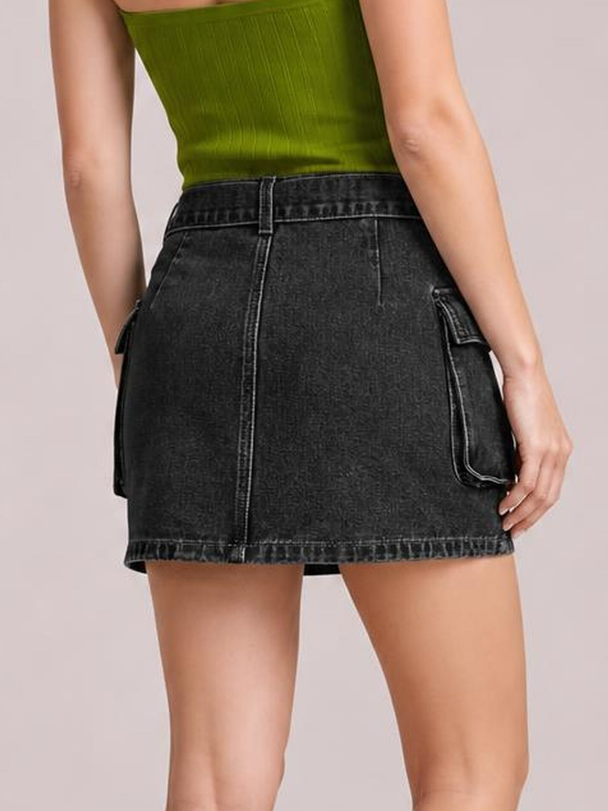A model stands from behind in a black denim mini skirt with a high waistband, belt loop, contrast stitching, center seam, and flap pockets.