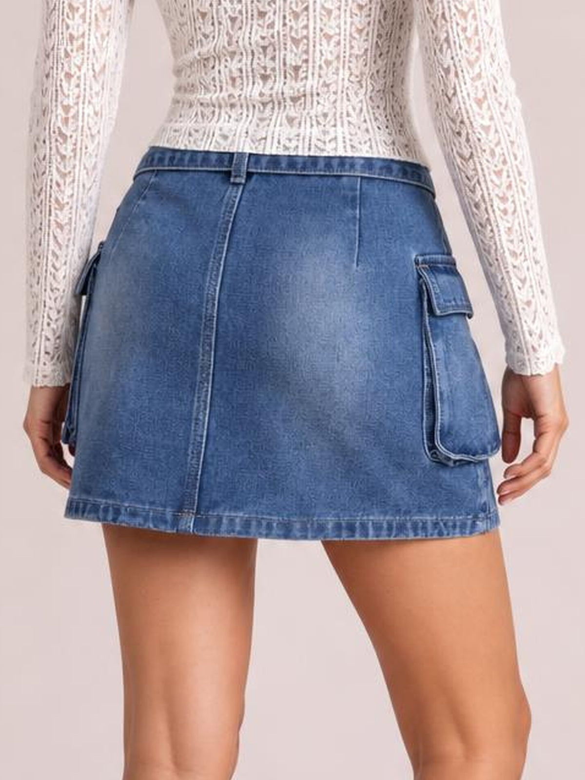 Model standing in a blue denim mini skirt with a fitted waistband, center-back seam, straight silhouette, raw-looking hem, and large side cargo pockets.