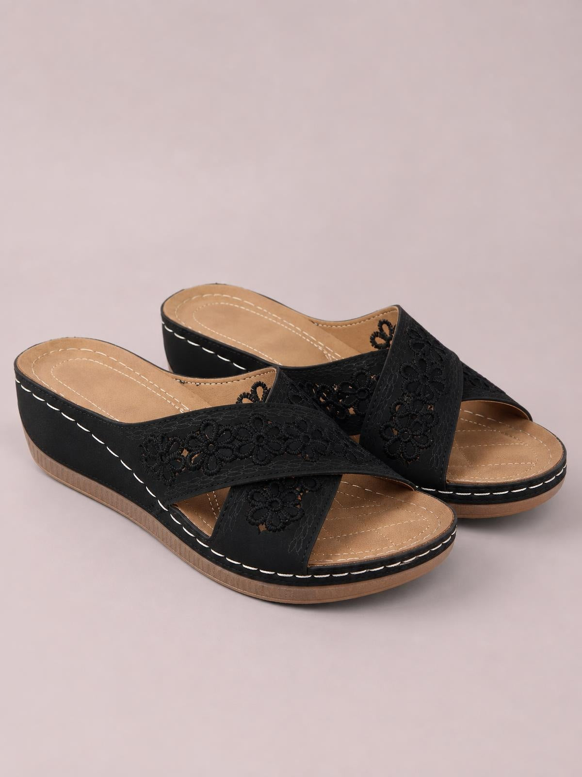 Black crisscross flower wedge sandals feature open toes, embroidered floral straps, tan cushioned footbeds, low wedge heels, and contrasting white stitching.