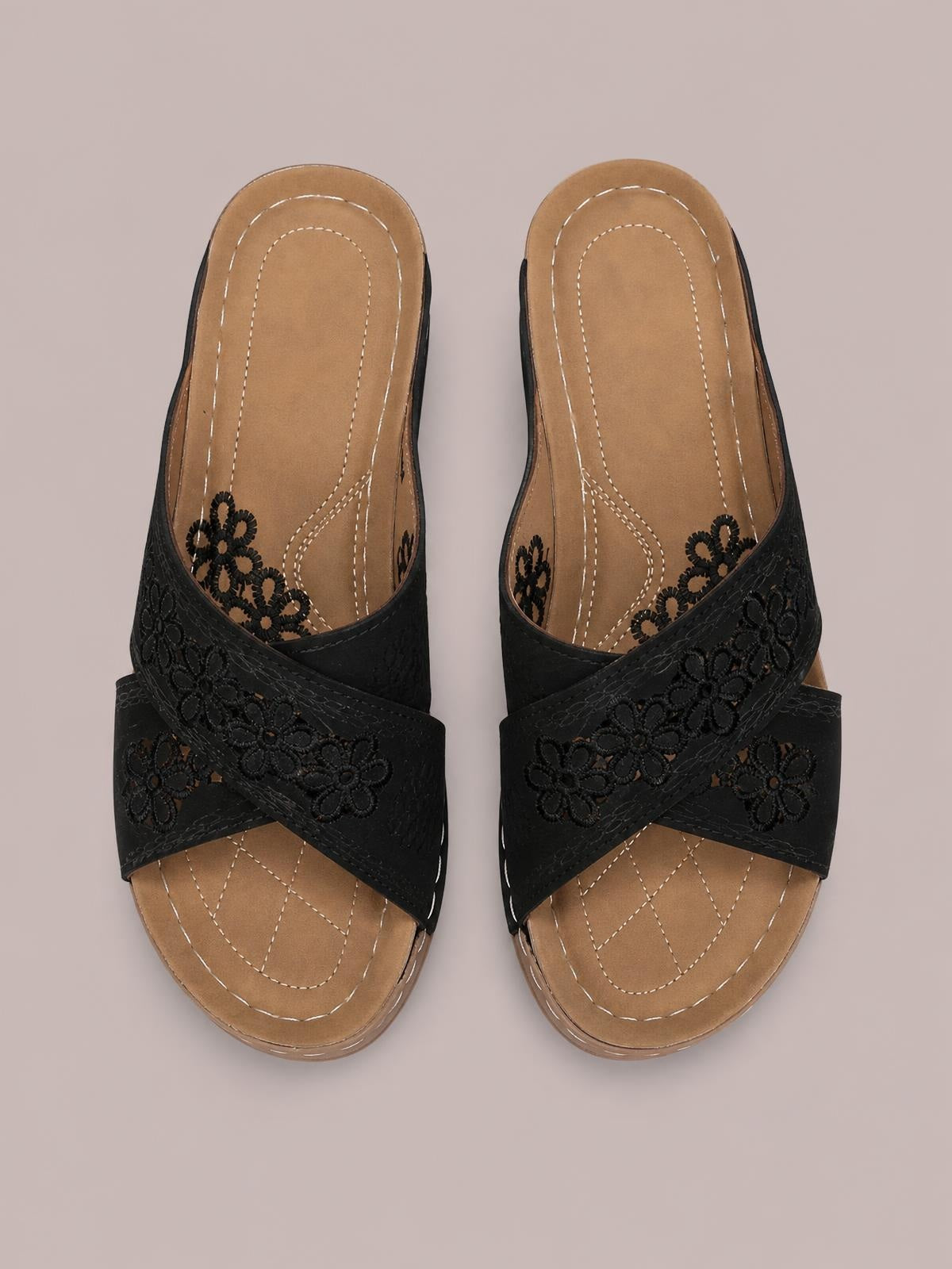 Black crisscross flower wedge sandals feature open toes, floral-embellished straps, tan cushioned footbeds, and a low wedge heel for comfortable everyday wear.