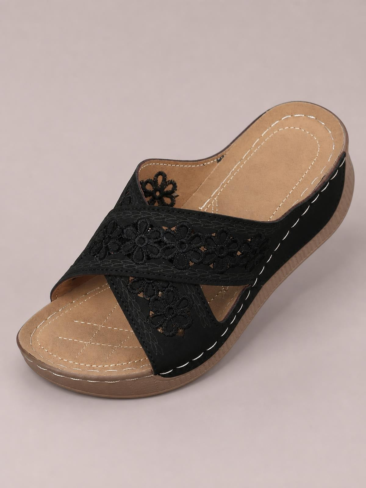 Black crisscross flower wedge sandals feature embroidered floral straps, an open toe, tan cushioned footbed, and a low wedge sole with contrast stitching.